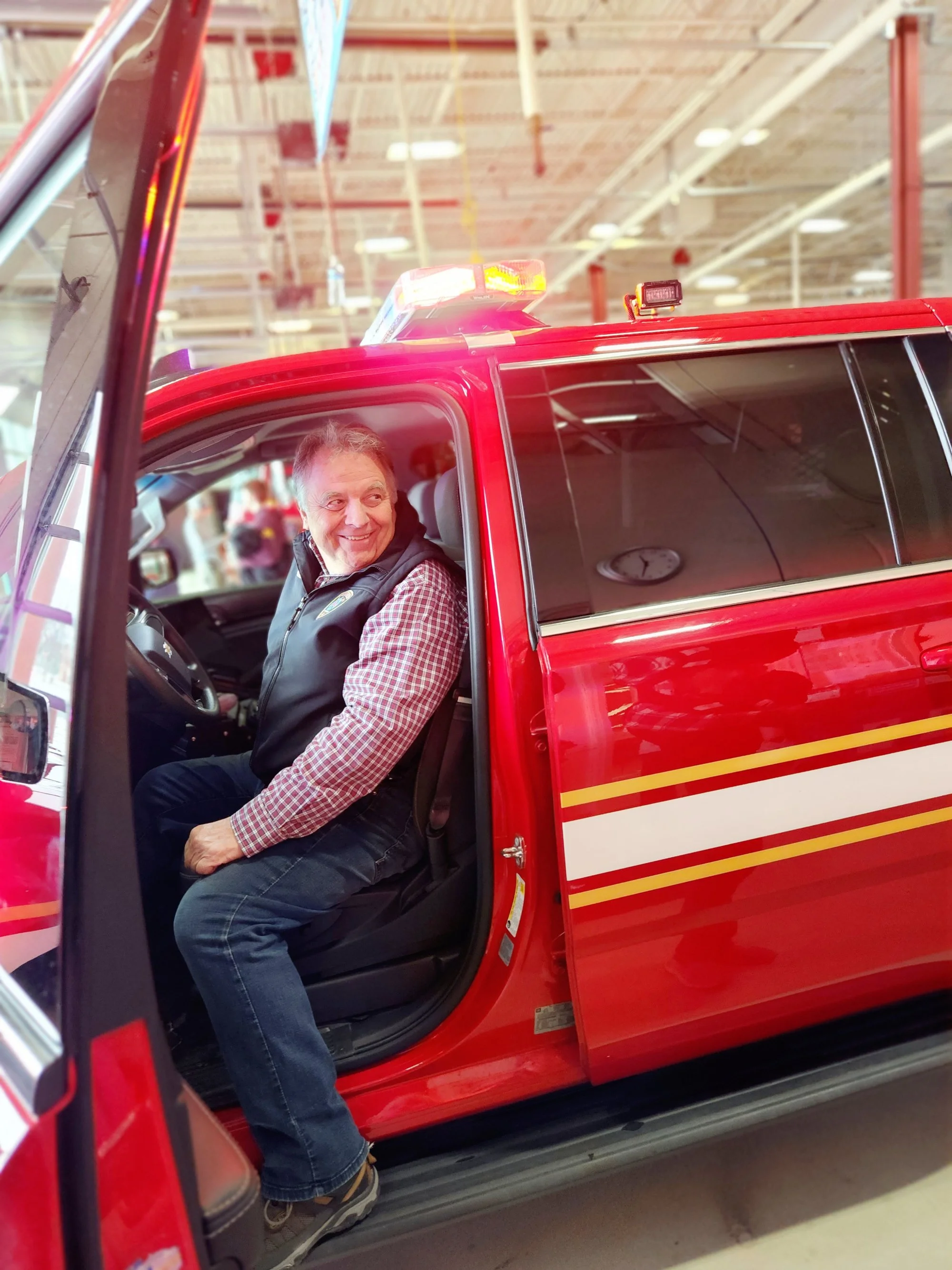 Greg Pederson sitting inside a red emergency vehicle with a smile, looking out of the open door inside the garage of the Mound Public Safety building.