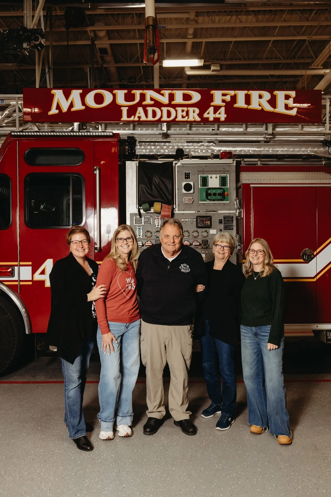 Greg Pederson, his wife Vickie, and their three daughters taking a family portrait in front of a fire truck with a sign that reads 'Mound Fire Ladder 44'.