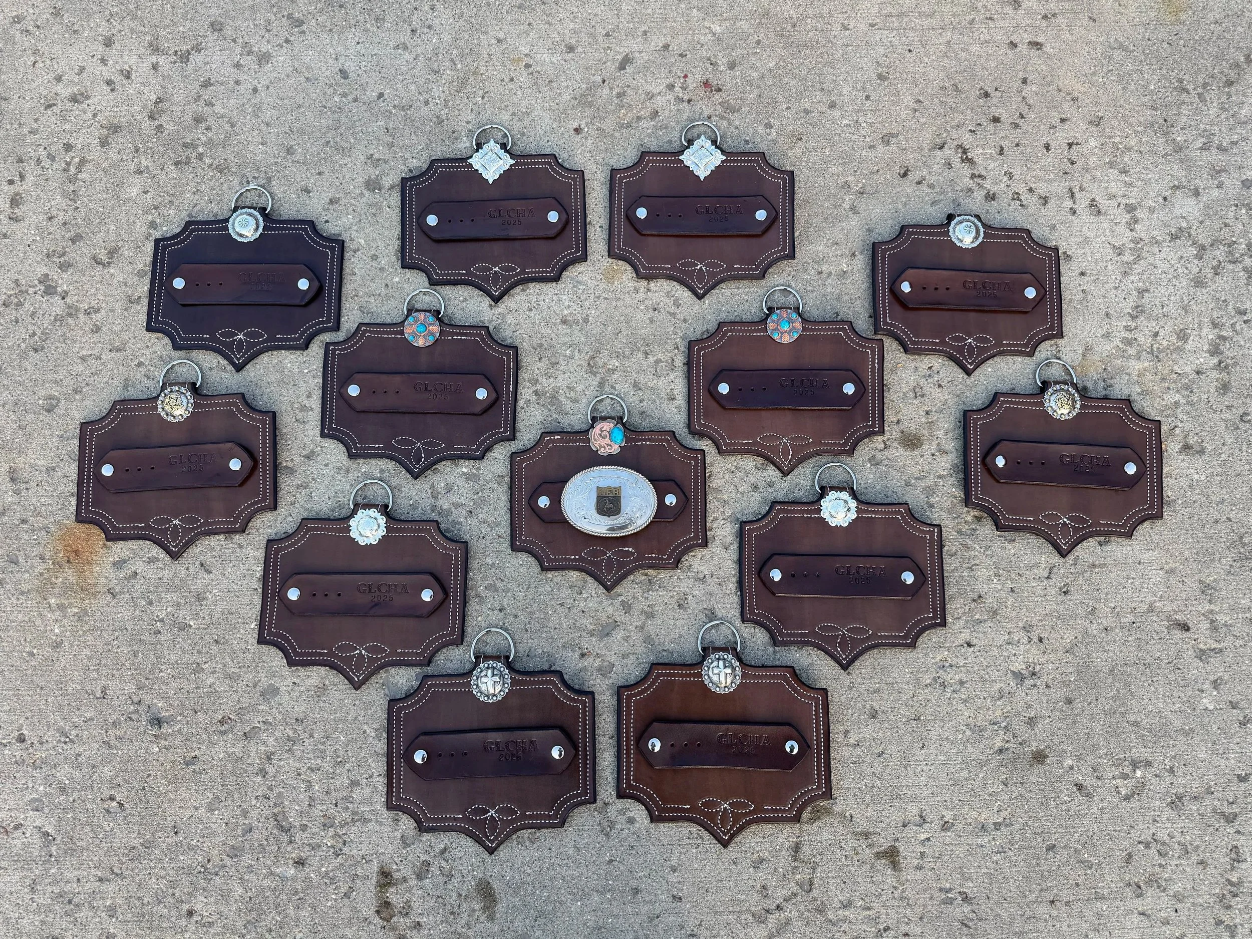 Collection of leather keychains on a concrete surface, each with different decorative charms or emblems.