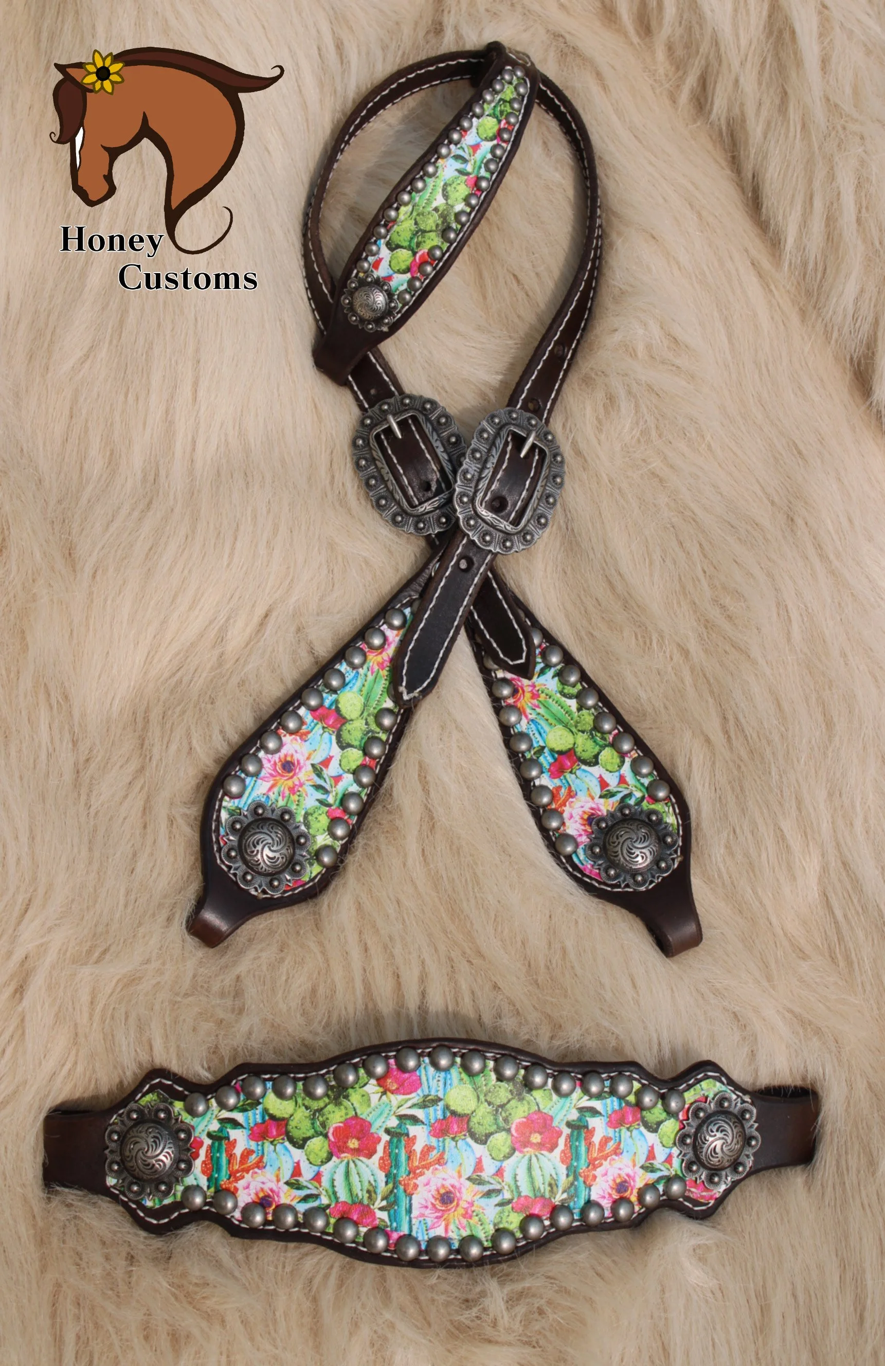 Close-up of decorative leather horse tack with floral fabric inlays and silver embellishments, laid on a soft, furry beige background.