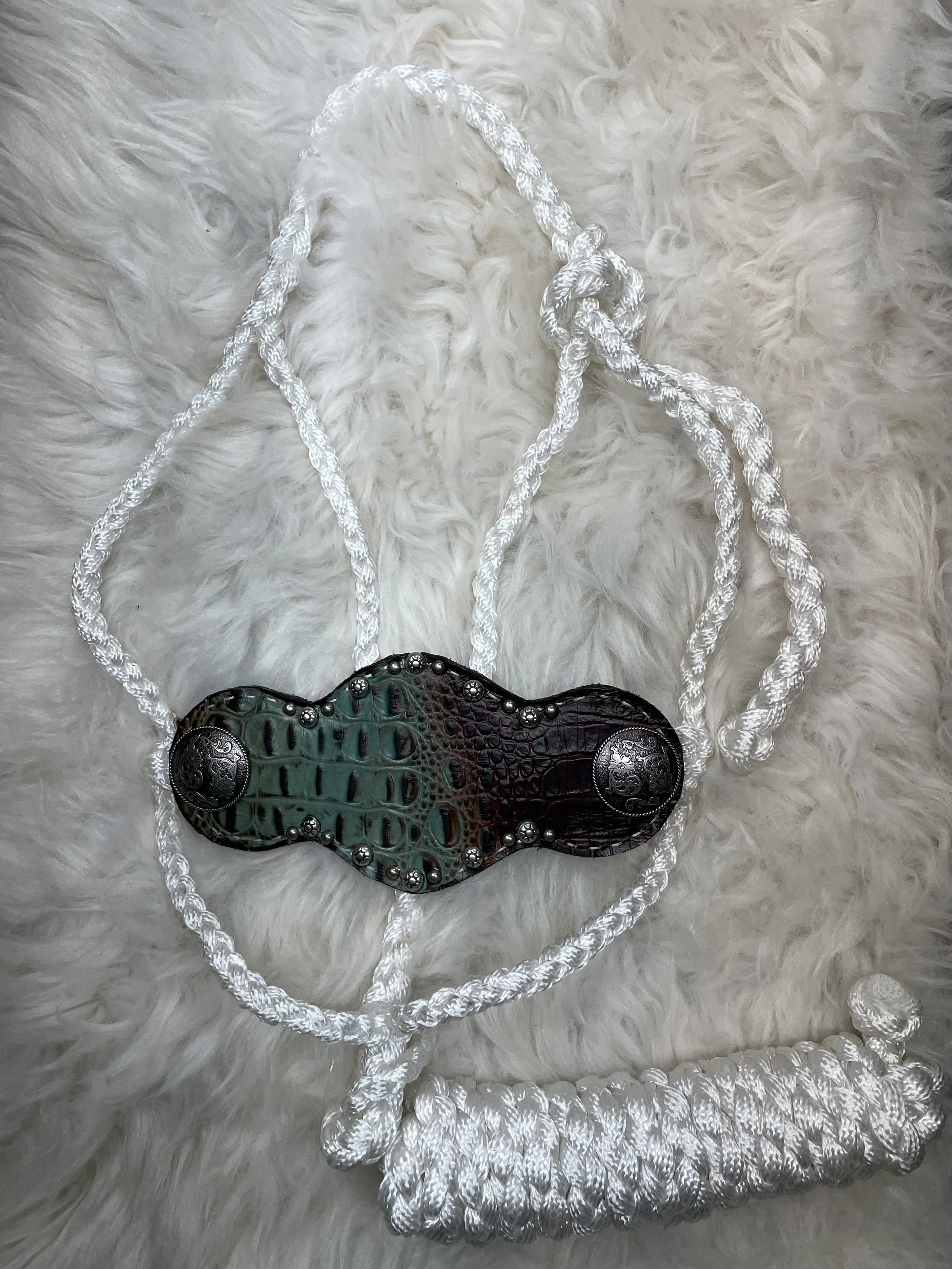 A decorative necklace with a pendant resembling a snake, resting on a white furry surface. The pendant features green and brown colors with metallic accents and intricate detailing.