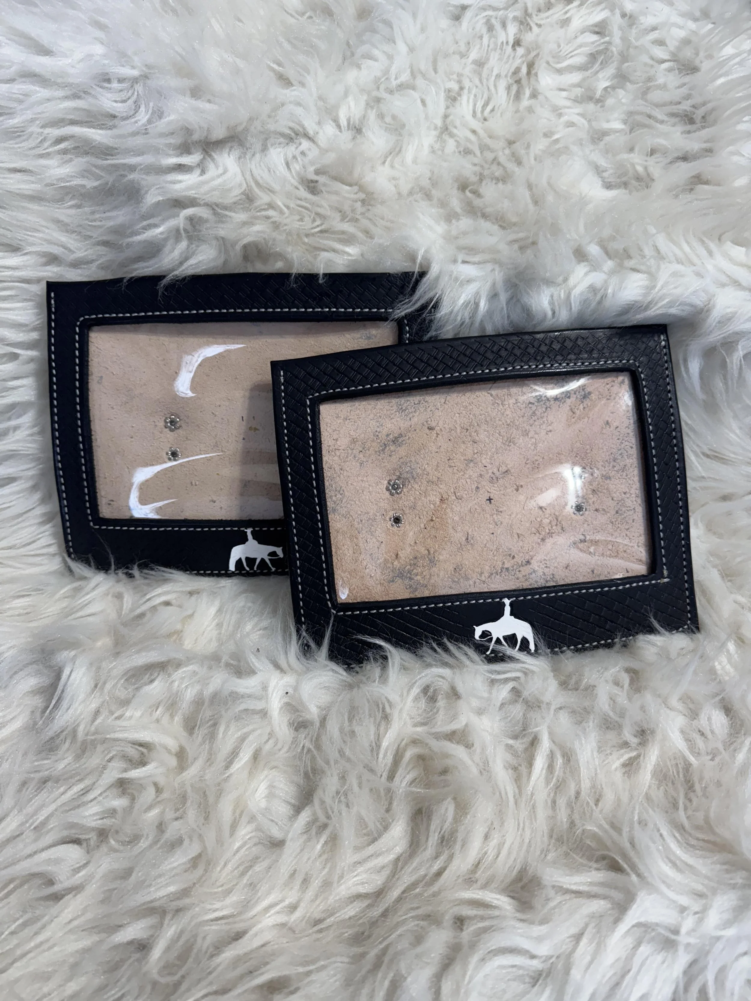 Two black photo frames with clear glass fronts displaying pictures, placed on a fluffy white rug.
