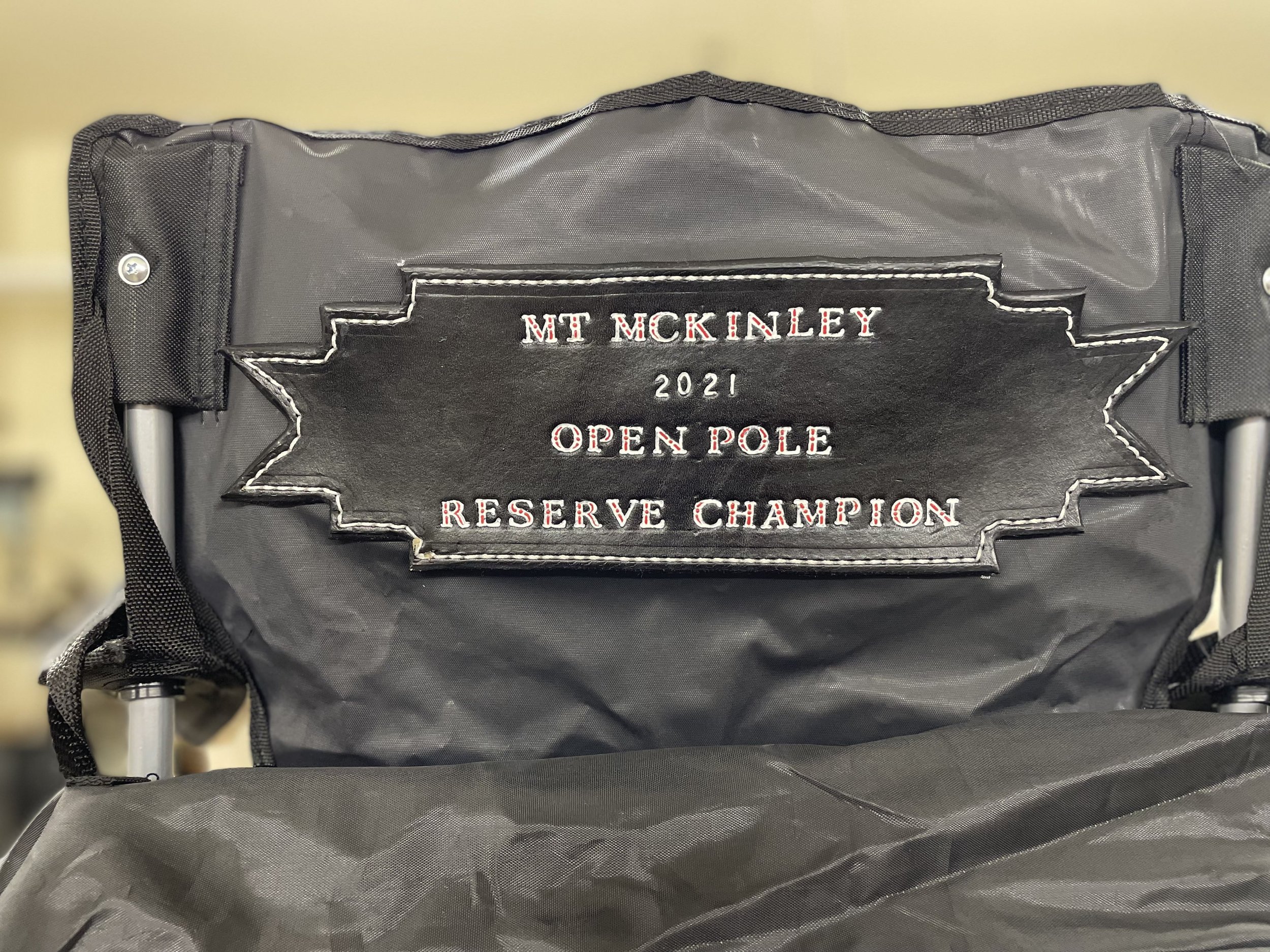 A black bag with embroidered text that reads 'MT MCKINLEY 2021 OPEN POLE RESERVE CHAMPION.' The bag is attached to a metal frame, and part of a strap is visible on the left side.