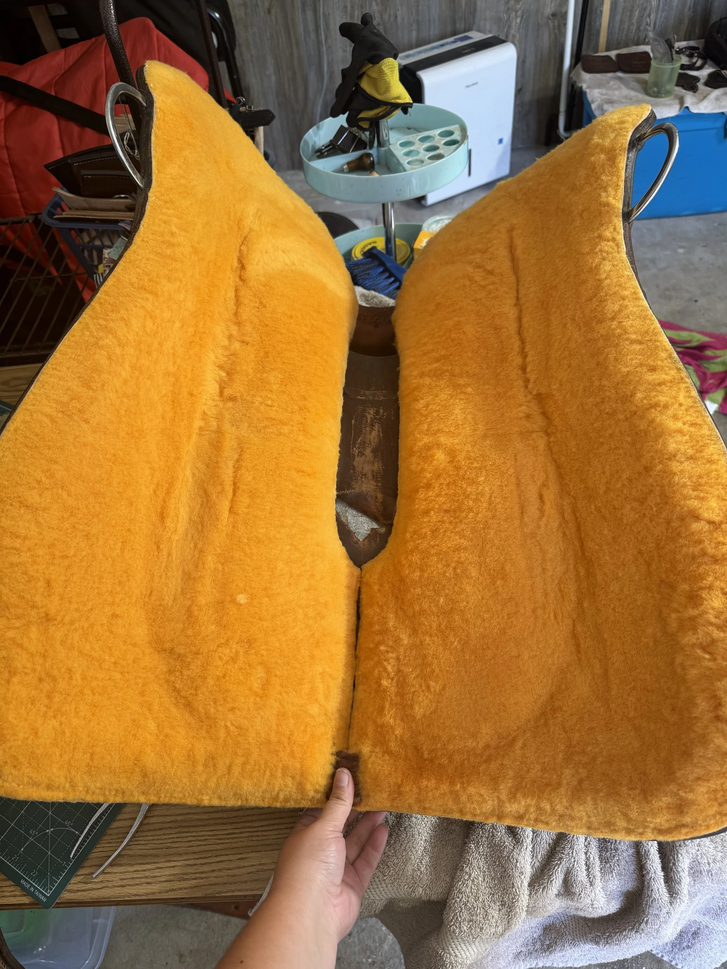 A person holding back a large, orange, plush fabric piece with their hand, revealing a small section of a hidden object underneath.