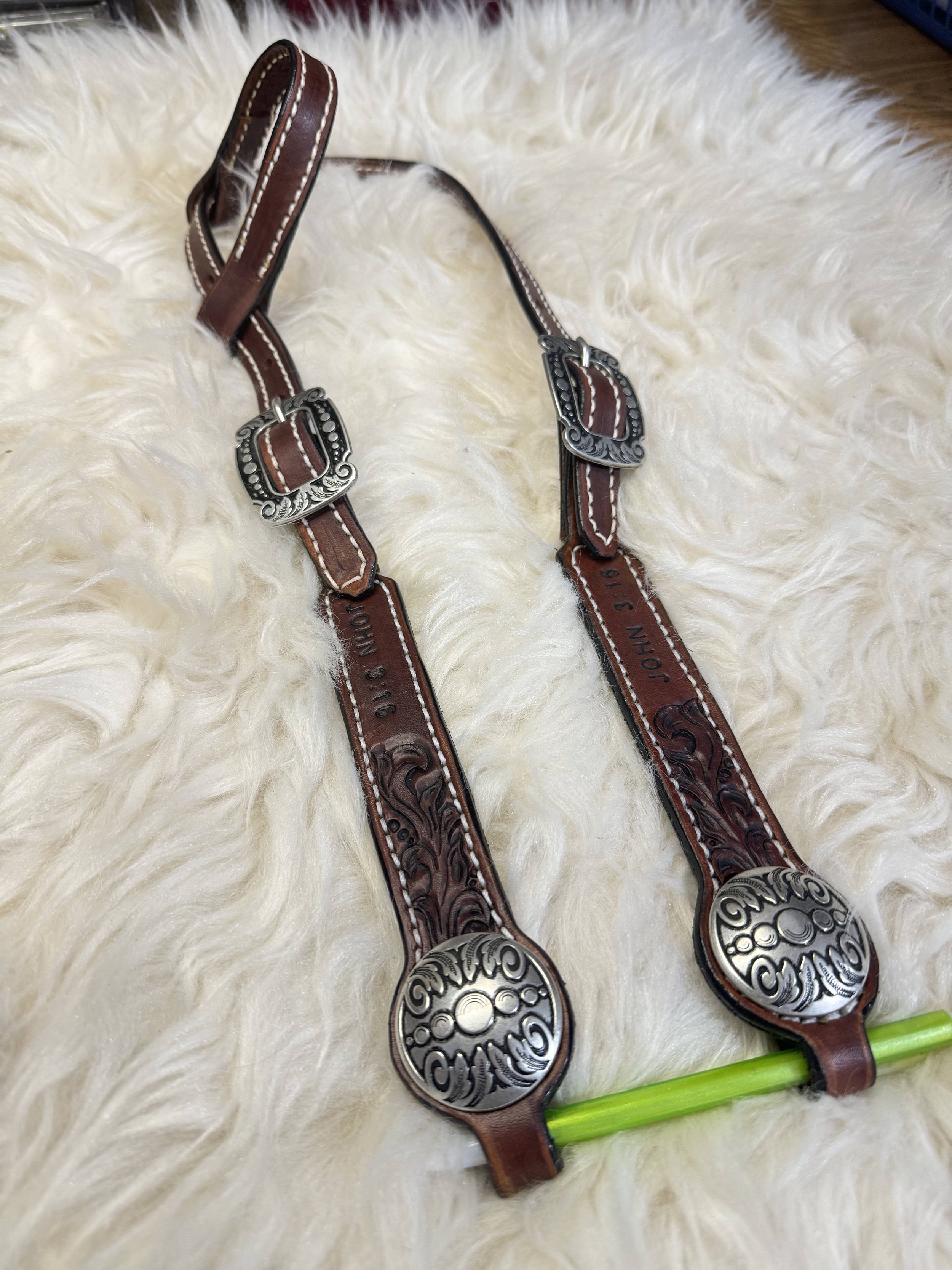 Two decorative leather and metal spoons with green handles resting on a white fluffy surface.