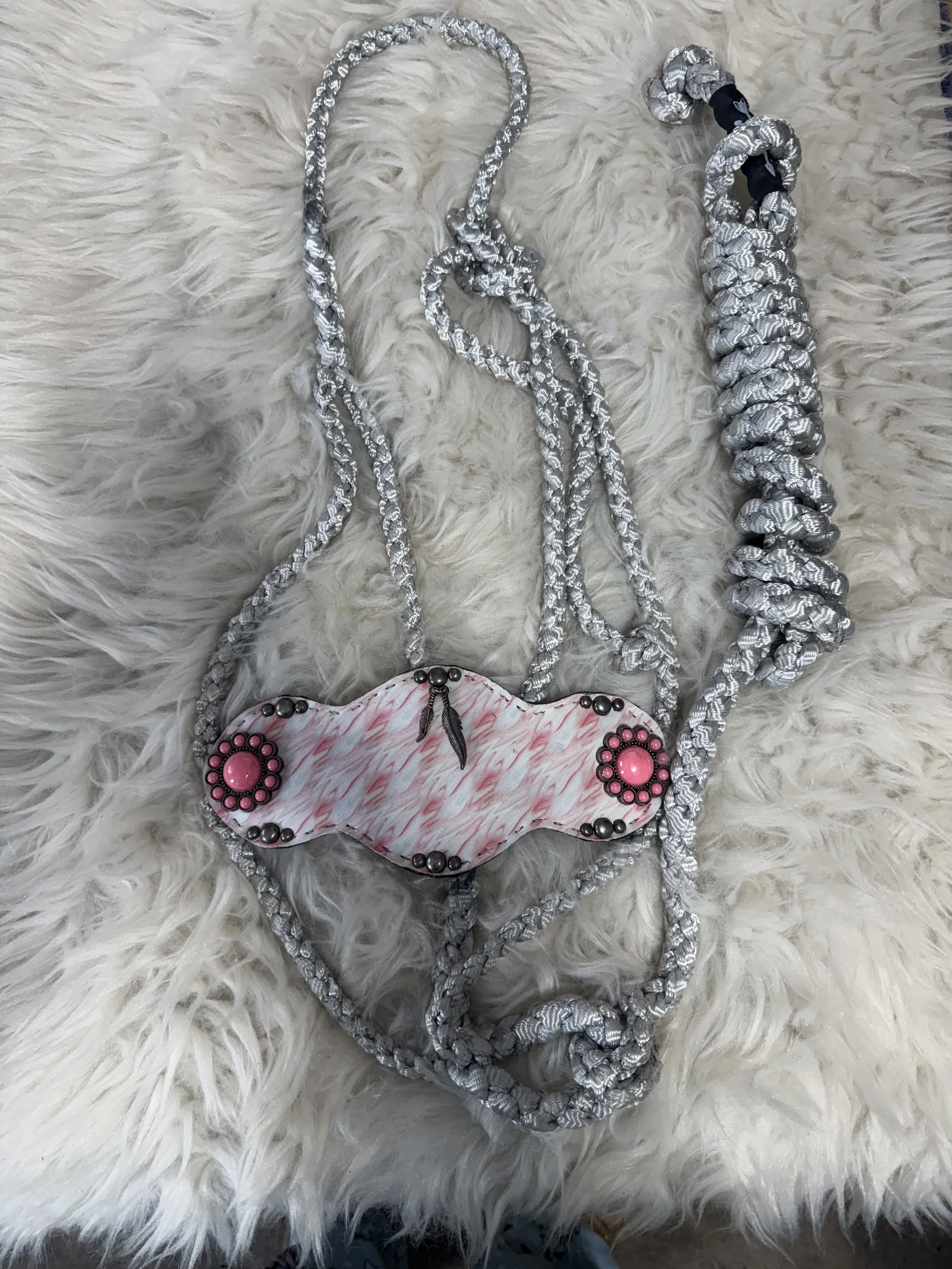 A fuzzy white surface with silver braided cords and pink and black decorative jewelry pieces with feathers and beads.