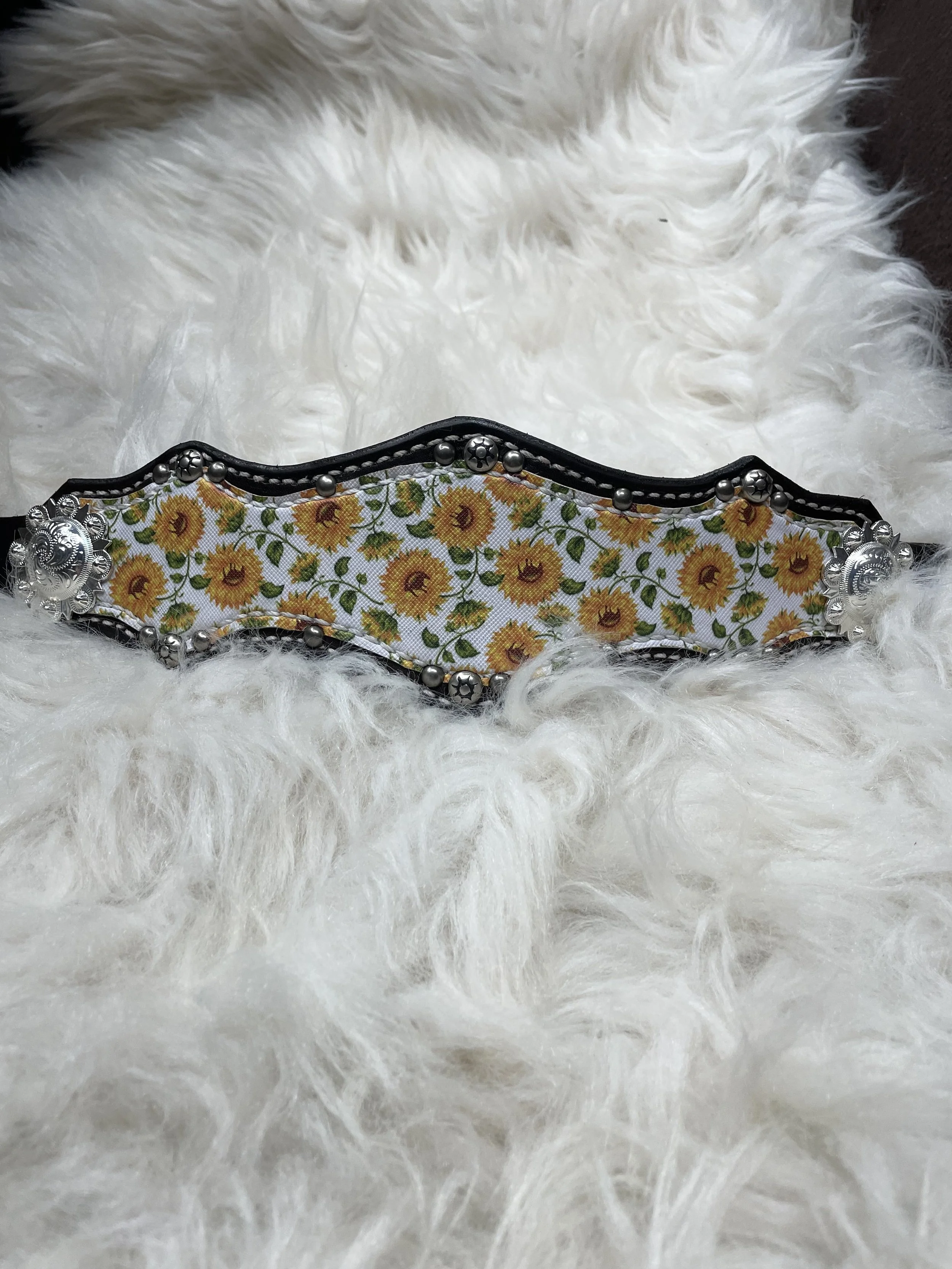 A decorative belt with sunflower pattern and silver embellishments, lying on a fluffy white surface.