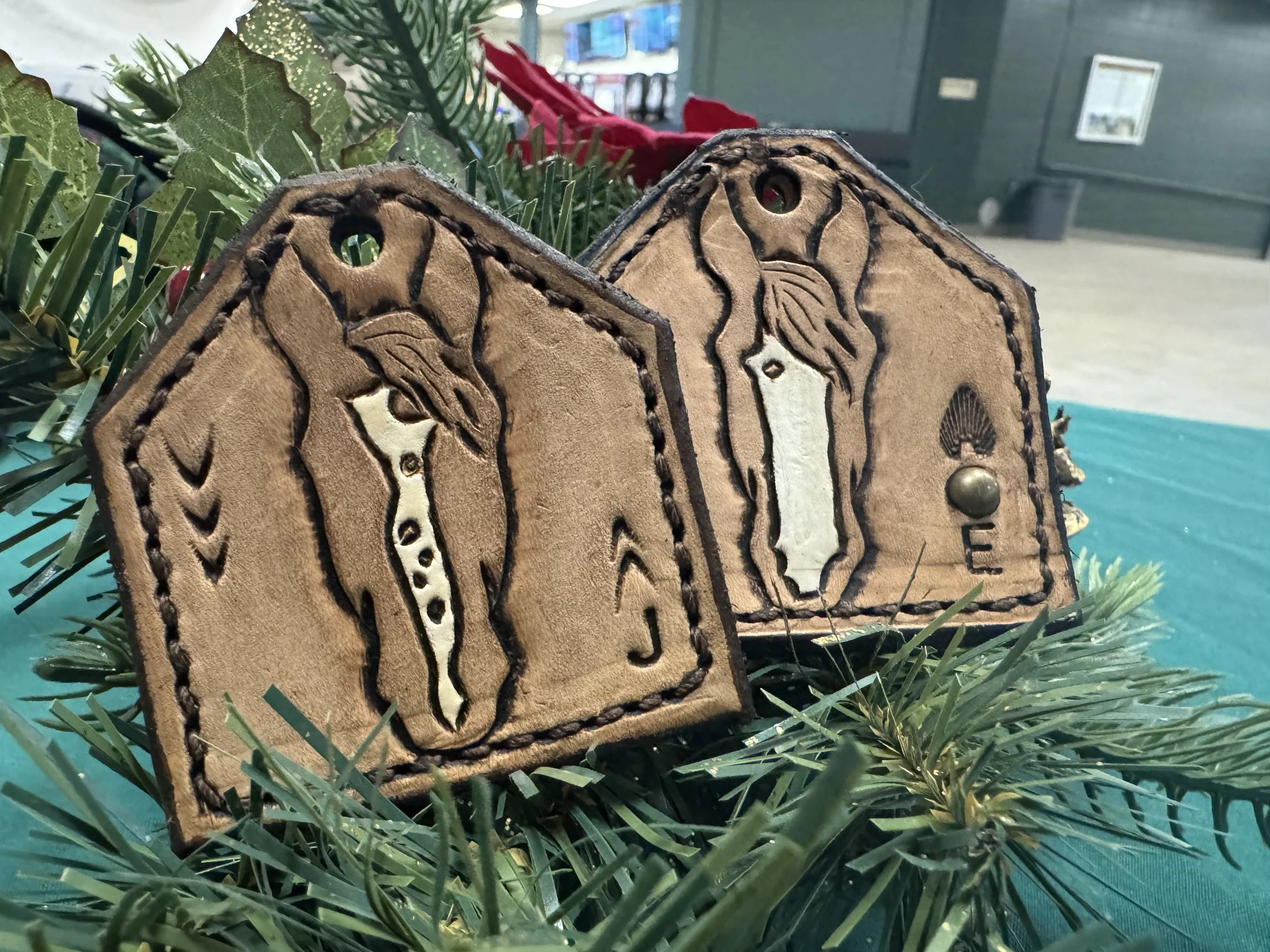 Close-up of a decorative wooden ornament with engraved animals and text, placed on green pine branches, with a blurred indoor background.