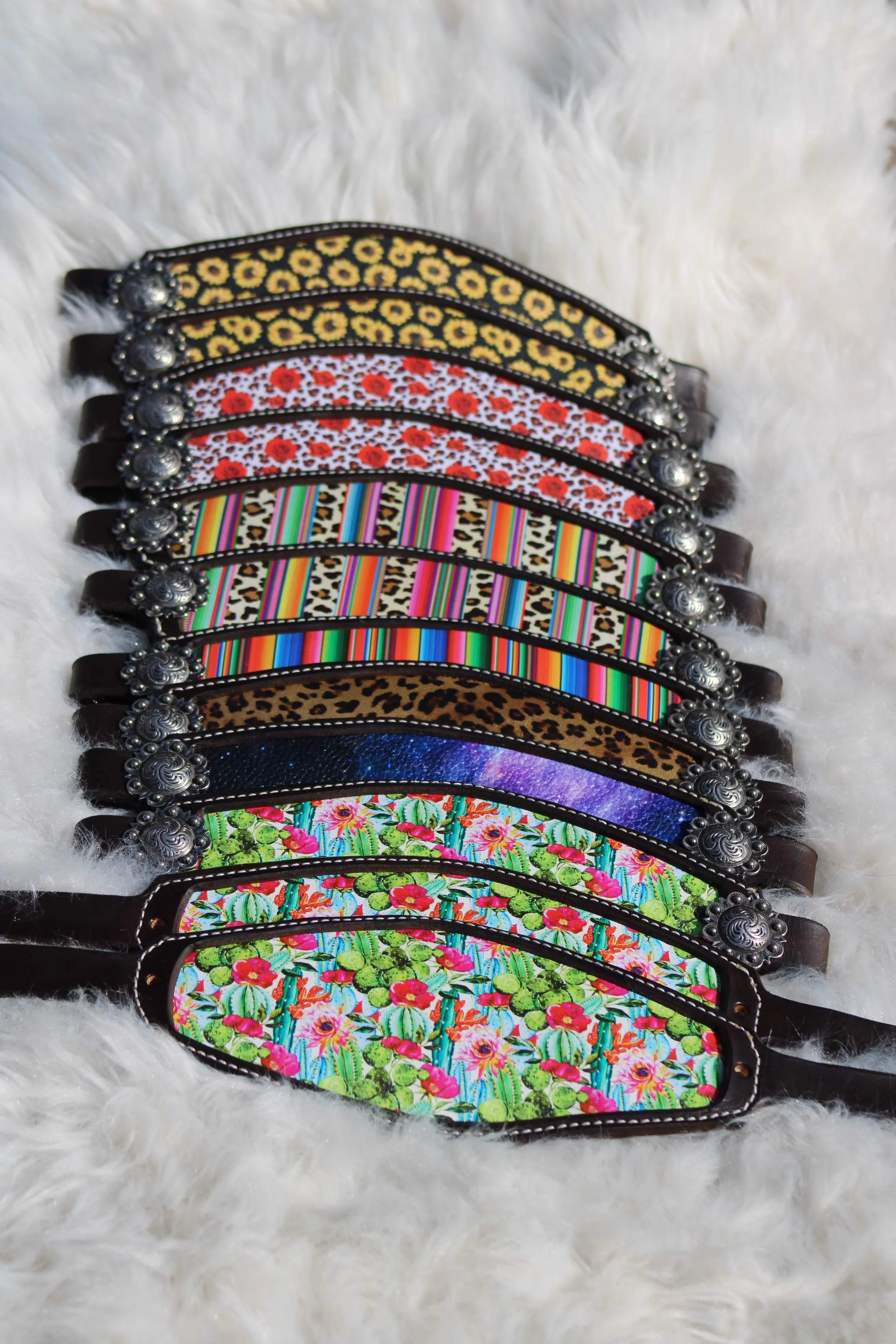 A collection of colorful dog collars with various floral and patterned designs, laid out on a white furry surface.