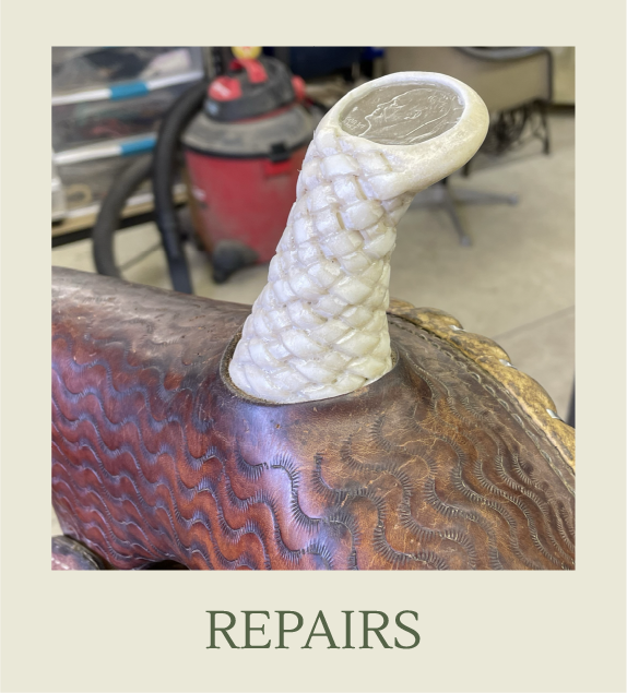 Close-up of an intricately carved metal saddle with a bone or ivory hoof pick resting on it, in a workshop setting.