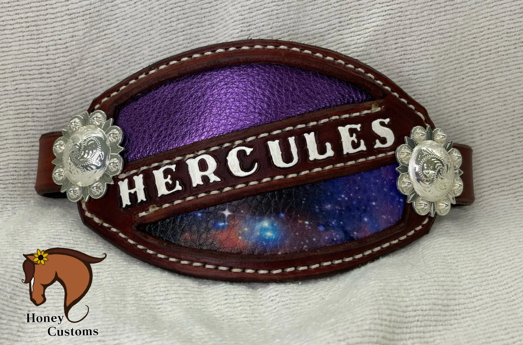A decorative dark red leather belt with silver conchos and a colorful cosmic galaxy design, featuring the word 'HERCULES' stitched in white letters across the front.