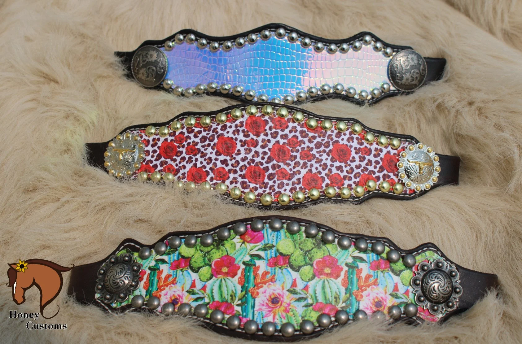Three decorative belts with metallic accents and colorful fabric patterns, placed on a furry surface.