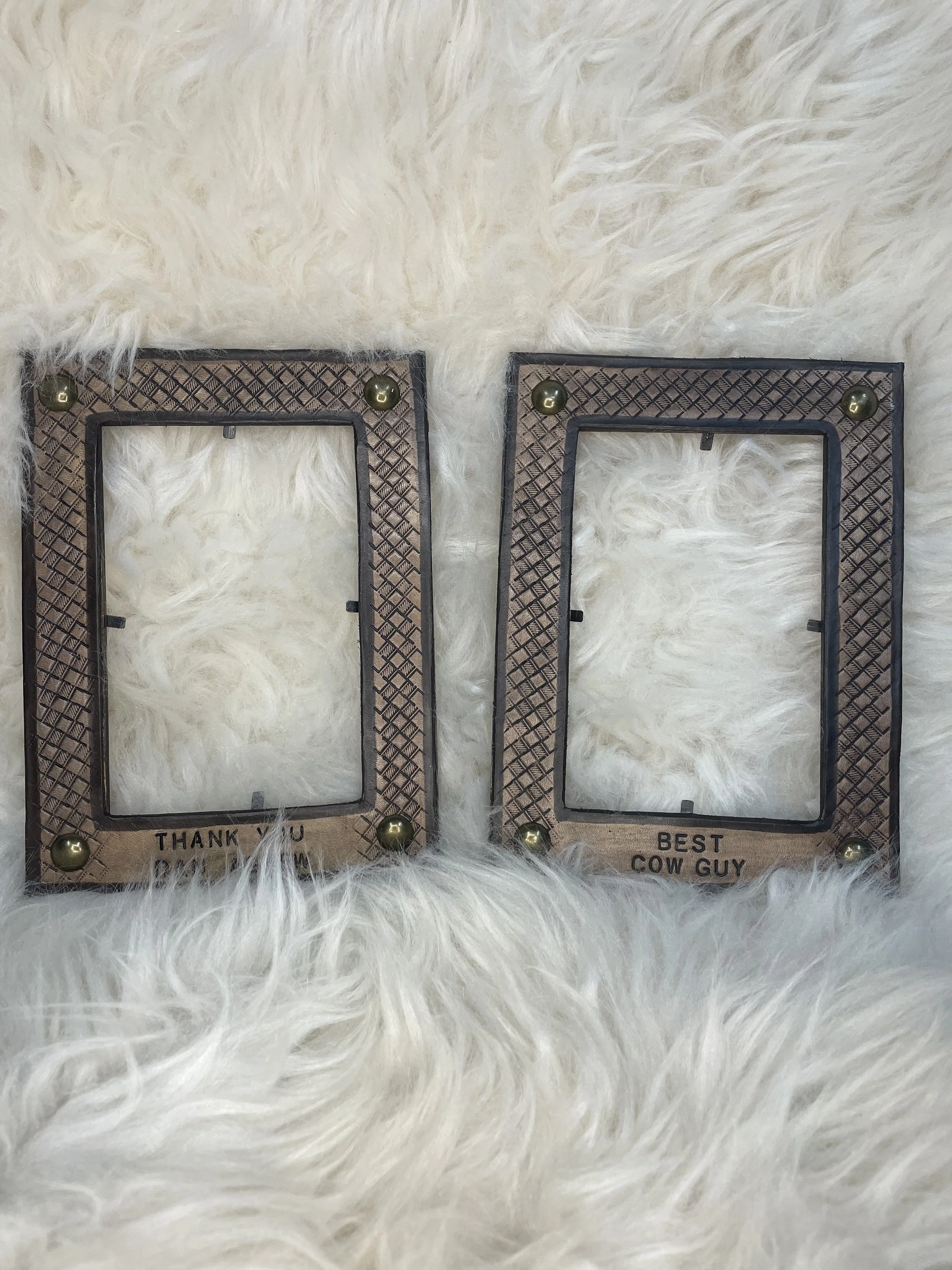 Two decorative photo frames with gold accents on a white furry surface. The frame on the left says "Thank You" at the bottom, and the frame on the right says "Best Cow Guy" at the bottom.