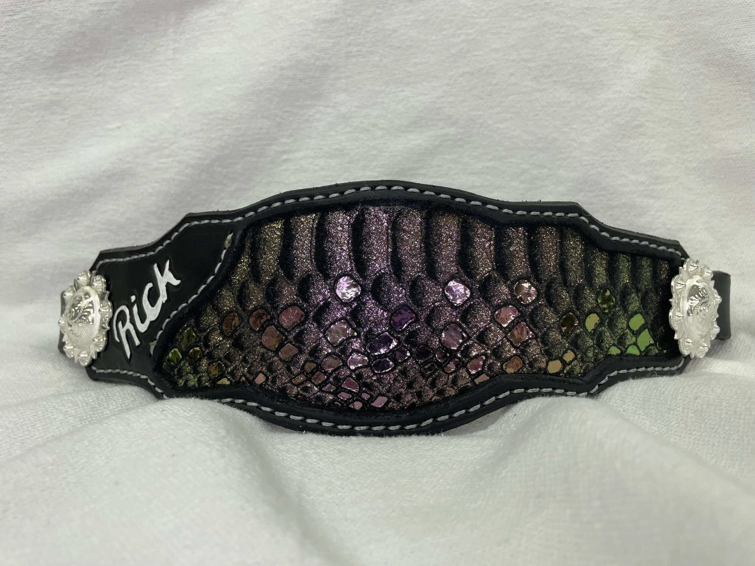 Close-up of a decorative black and purple clutch purse with rhinestones and pearl accents on a white fabric background.