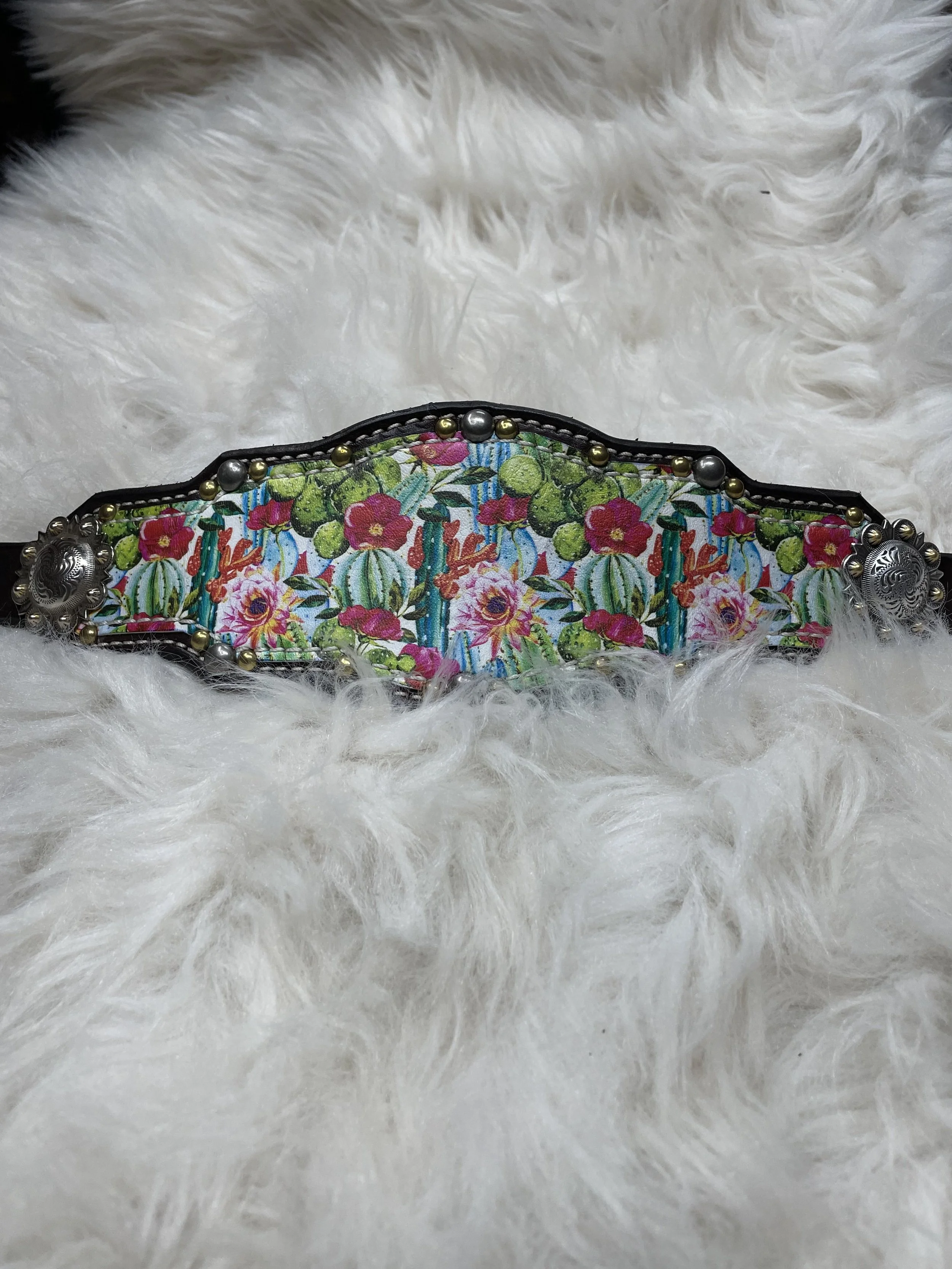 A belt with colorful floral and cactus pattern, decorated with silver and gold beads, resting on white fluffy fur surface.