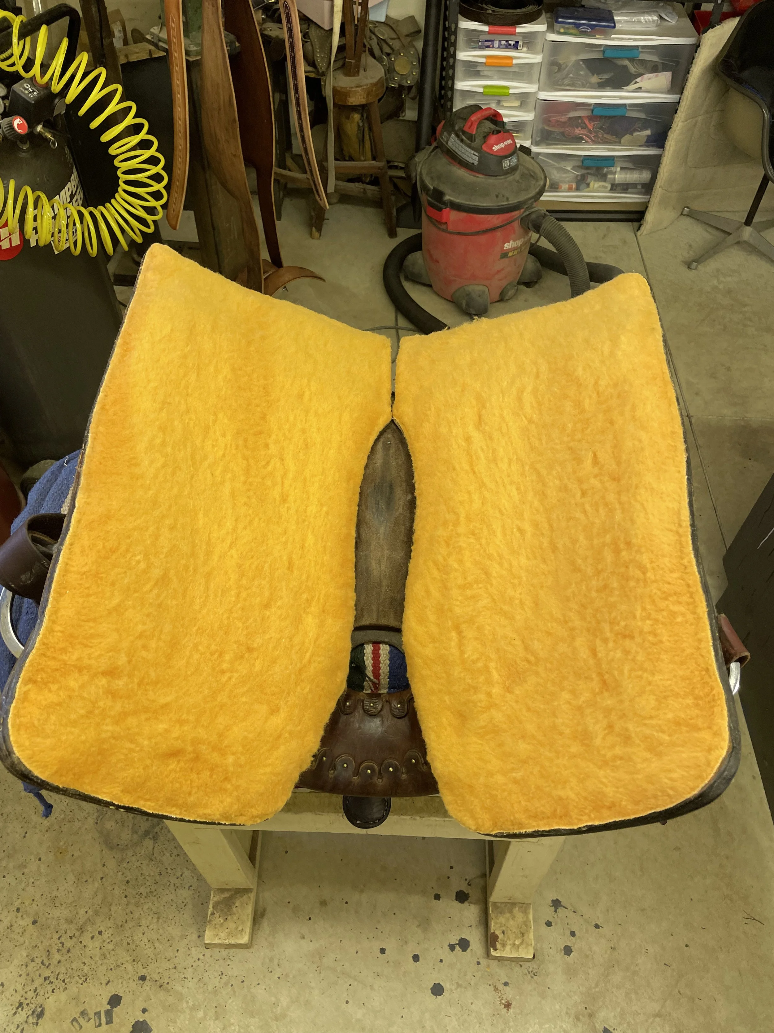 The image shows a person sitting on a chair with legs stretched out, wearing brown boots, with a large, yellow, textured block in front of them, creating a visual illusion of the block being the person's legs.