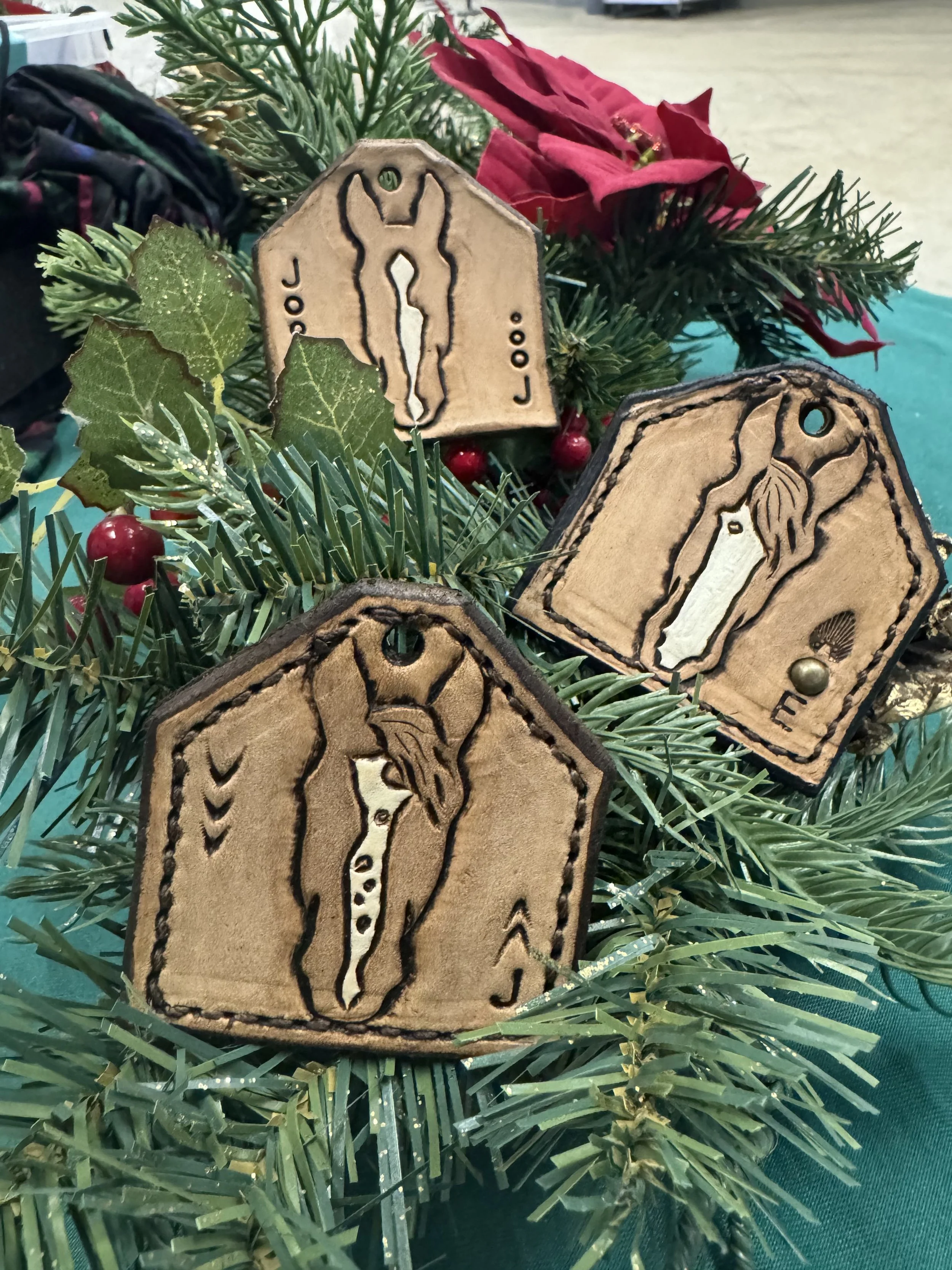 Close-up of Christmas decorations featuring faux wooden ornaments with horse silhouette engravings, green pine branches, artificial red poinsettia flowers, and red berries.