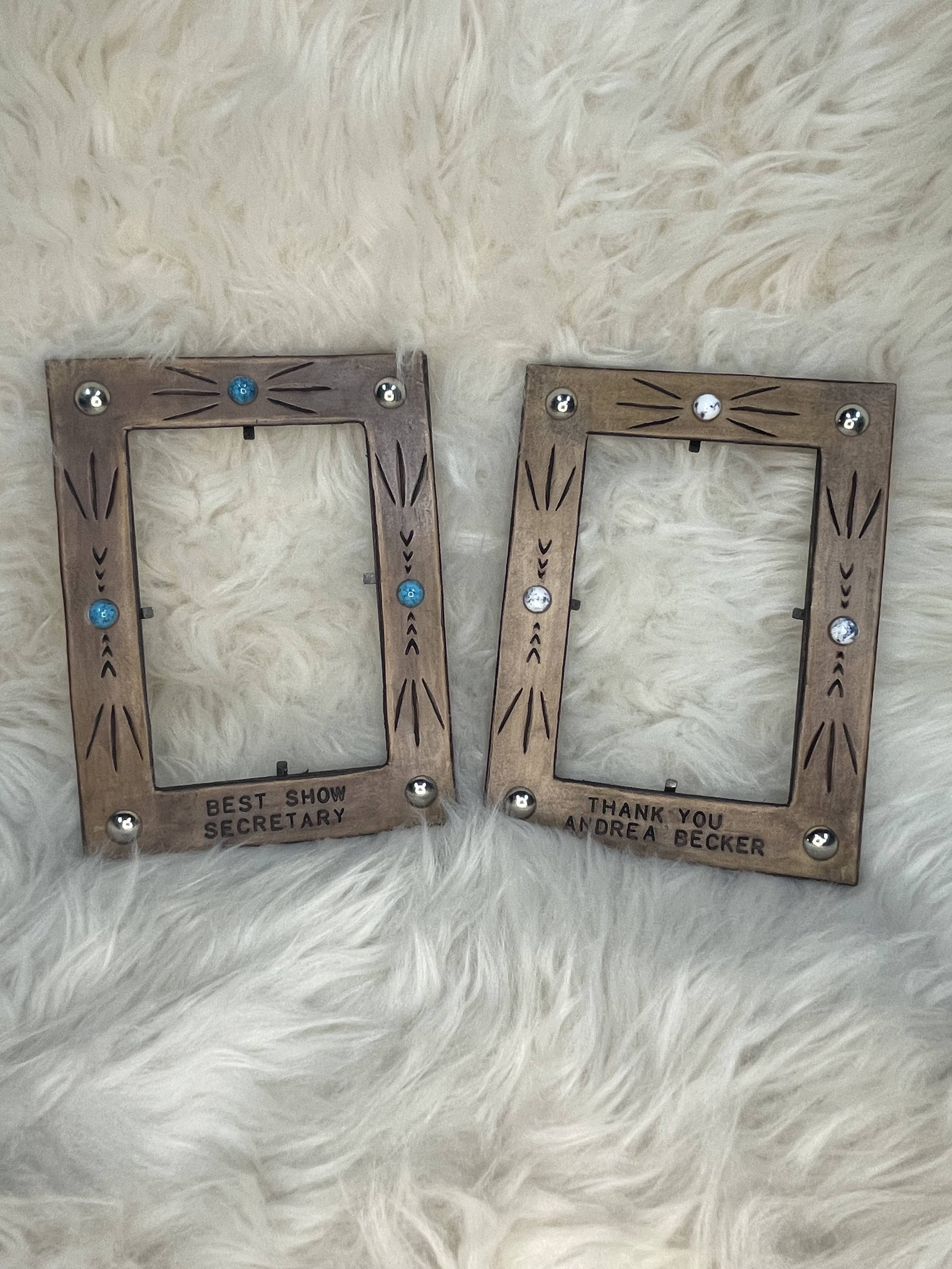 Wooden photo frame with decorative engravings and row of small rhinestones. The frame is personalized with engraved text, with one side reading 'BEST SHOW SECRETARY' and the other 'THANK YOU ANDREA BECKER'. It is placed on a soft, white, fluffy surfa
