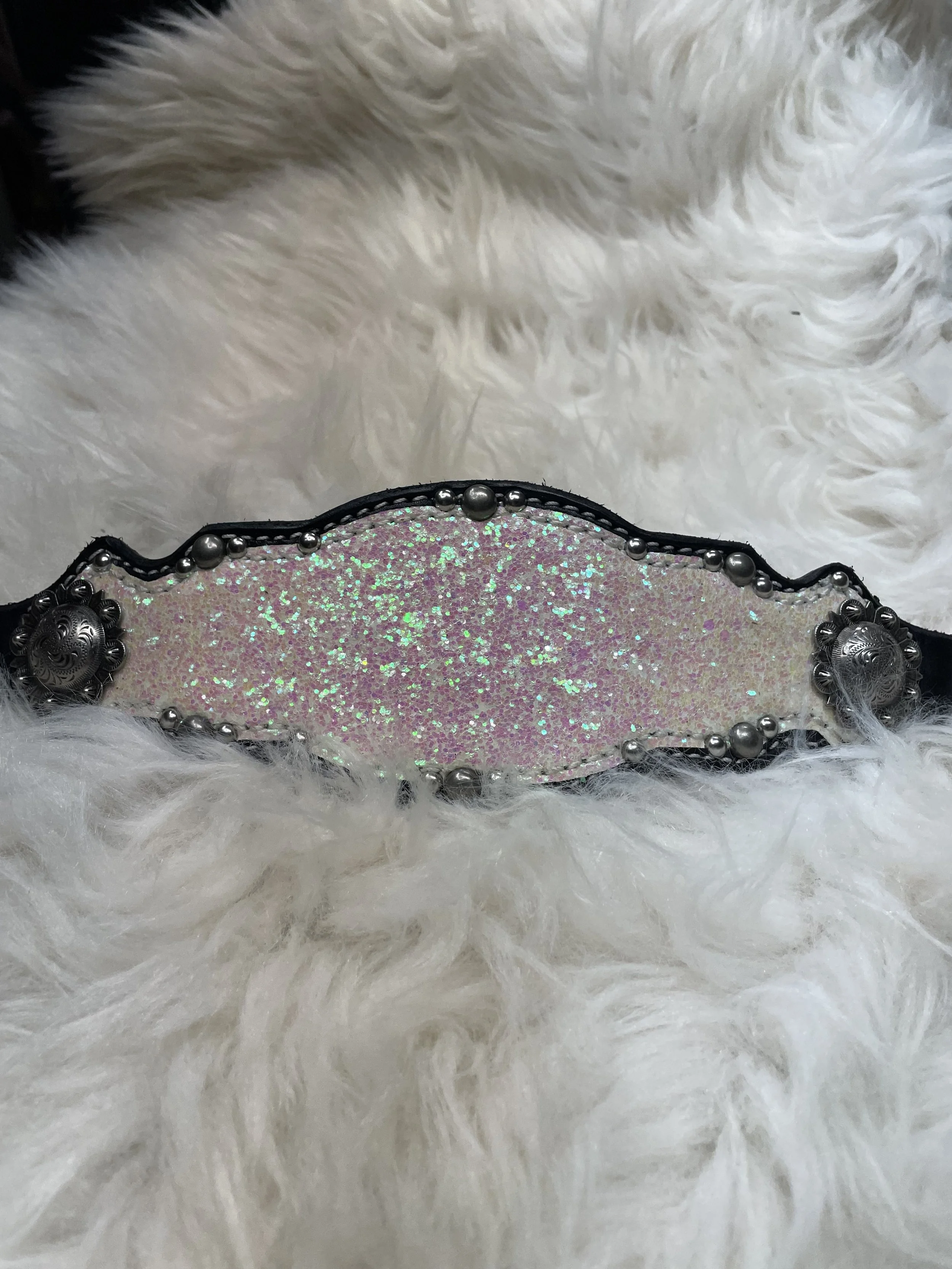 A decorative belt with pink glitter and silver embellishments, placed on a white fluffy fur background.