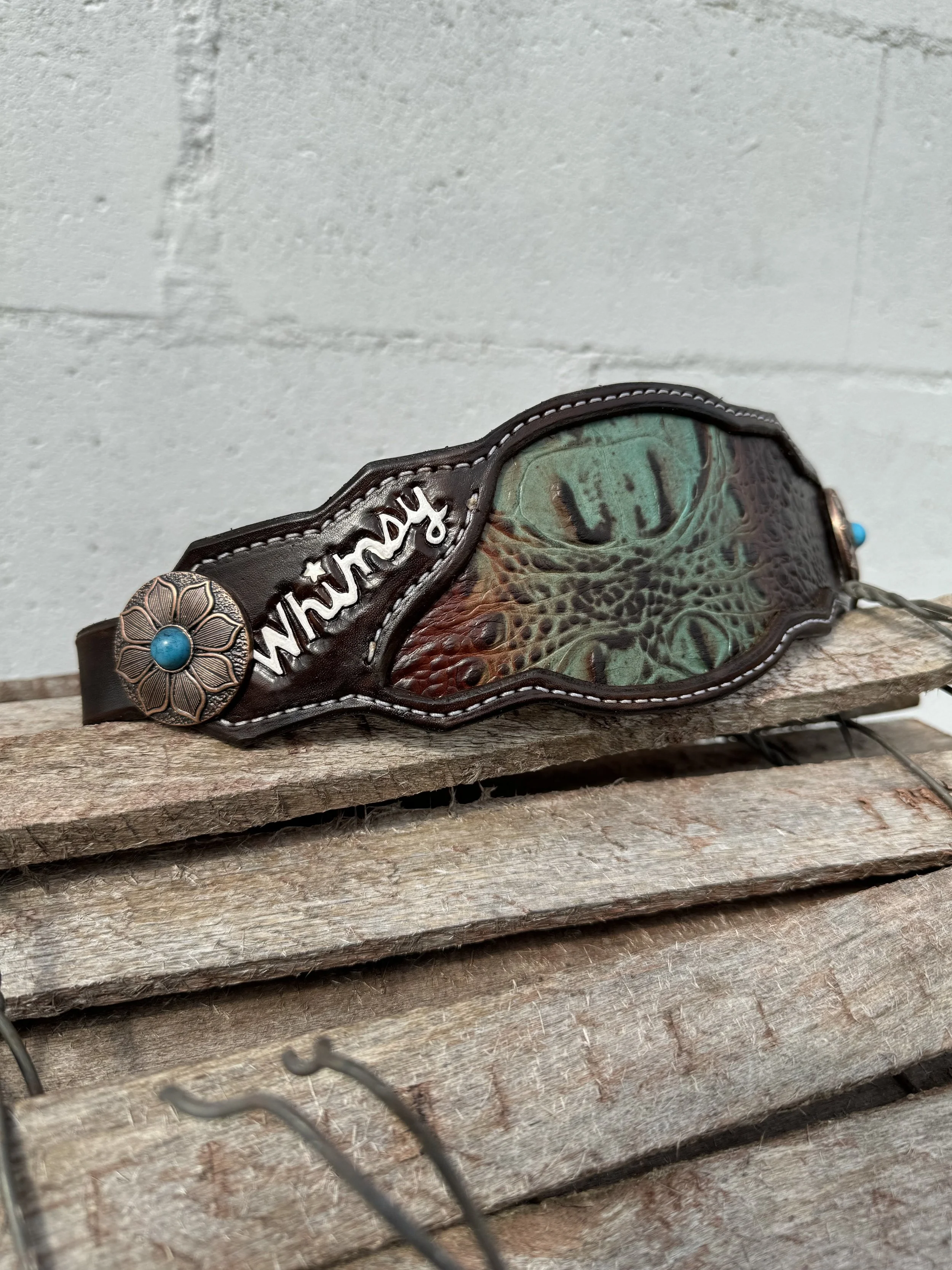 A decorative eyepatch with a lizard design and a metal flower emblem with a blue center, resting on a weathered wooden surface.