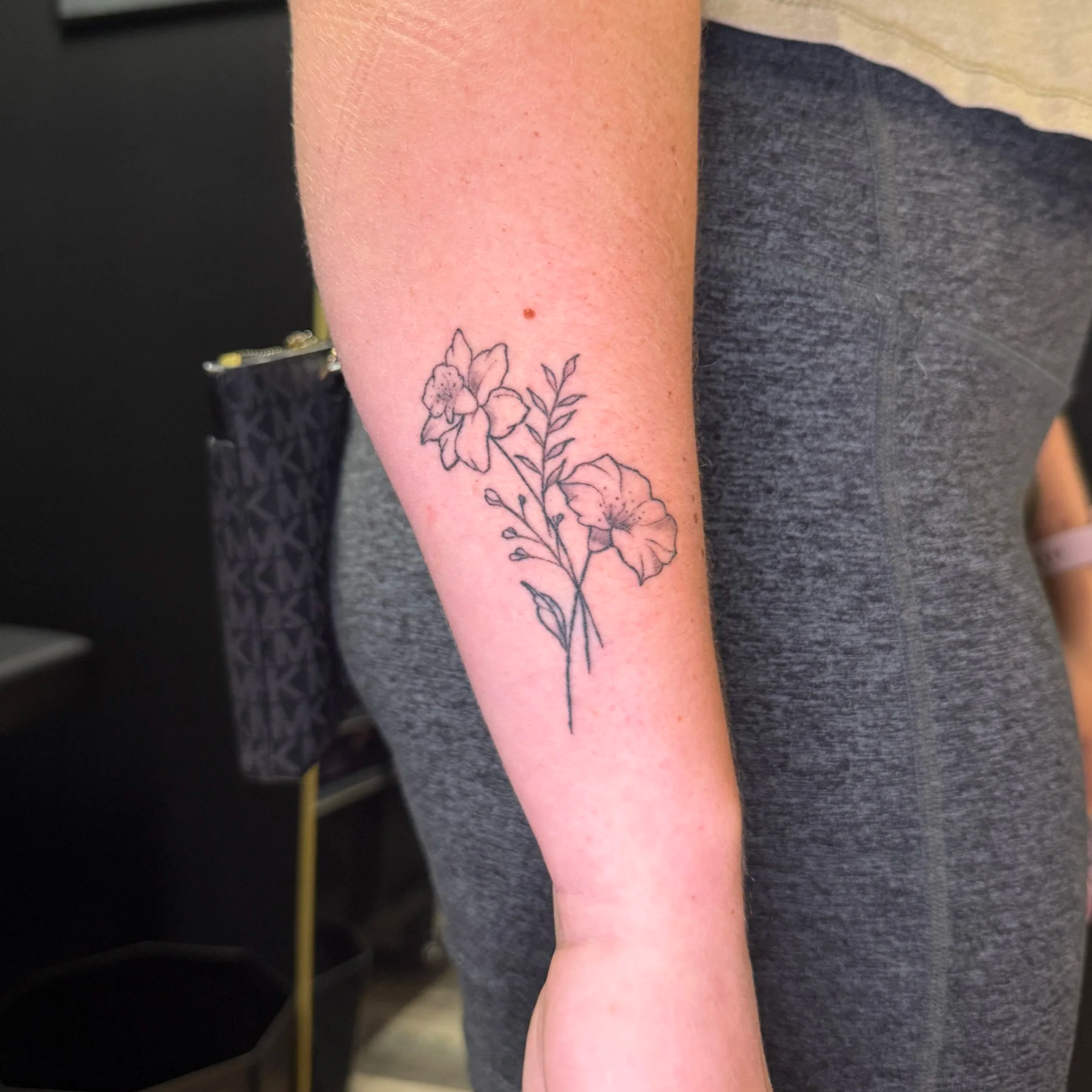 A person's forearm with a floral tattoo near the wrist, and a small mole on the skin.