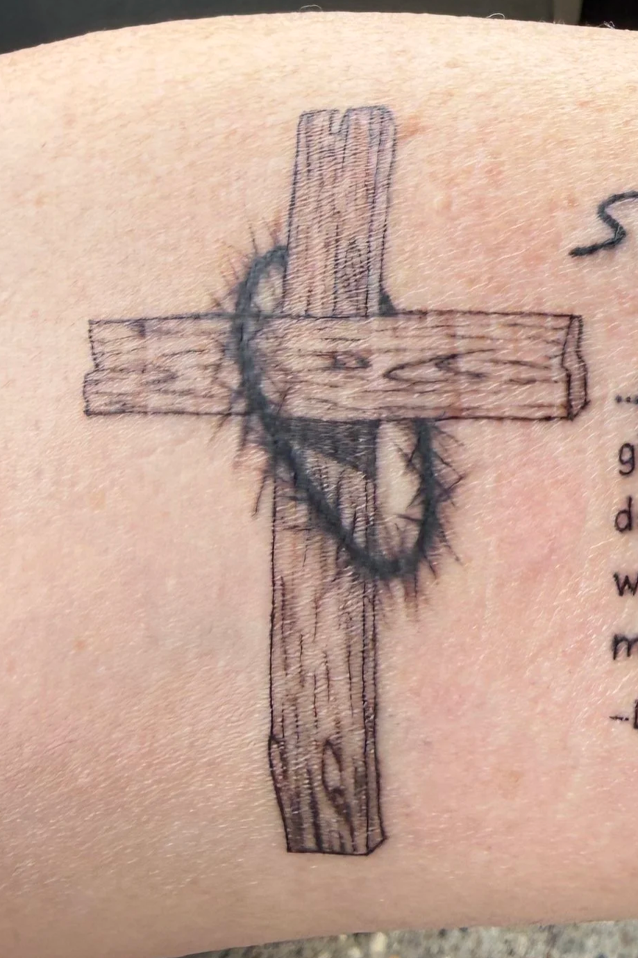 Tattoo of a wooden cross with a crown of thorns wrapping around it.