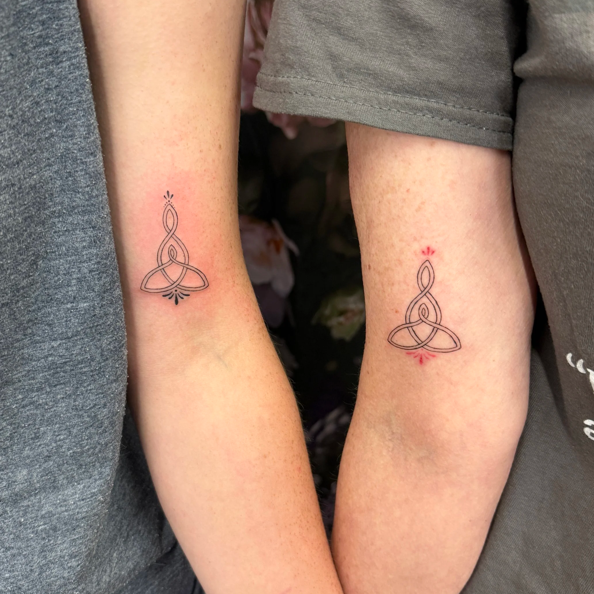 Close-up of three person's upper arms with tattoos, wearing gray and beige shirts.