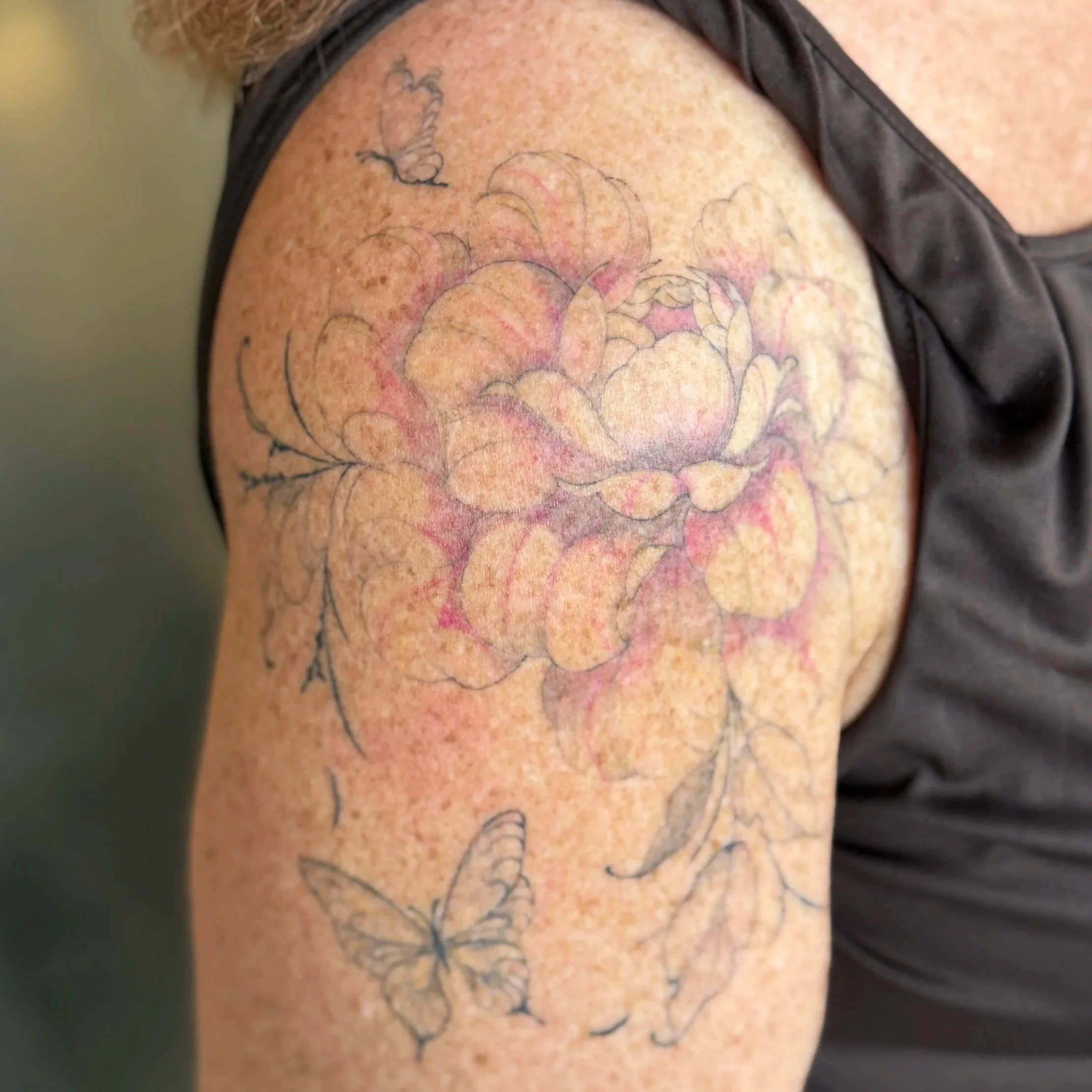 Close-up of a person's shoulder with a colorful floral tattoo and a small hummingbird tattoo.
