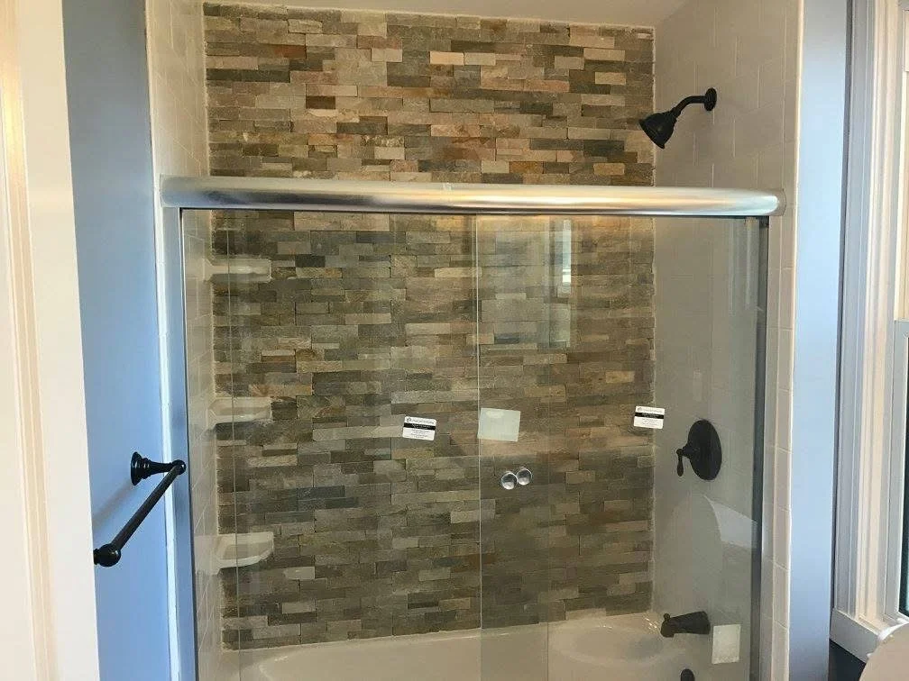 A modern shower with a glass door, black fixtures, and a stone tile accent wall.