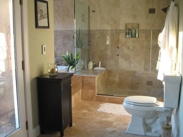 A bathroom with a walk-in shower with glass doors, a white toilet, a black cabinet, and a small countertop with decor, including a plant, in a well-lit room with beige tiled floors and walls.
