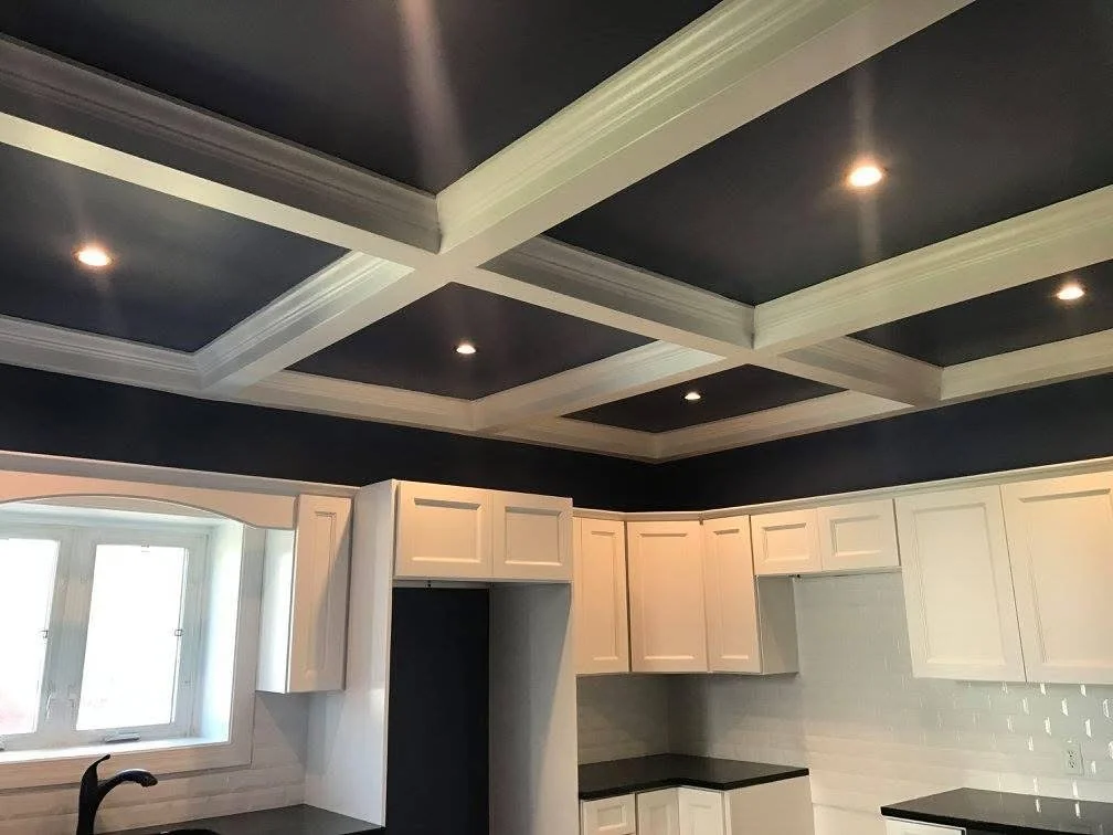 Interior kitchen with white cabinets, black countertops, a window, and a coffered ceiling with recessed lighting.