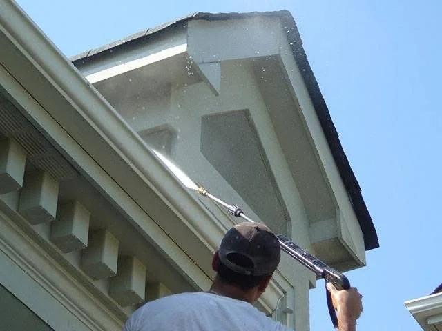 A person pressure washing the roof of a house