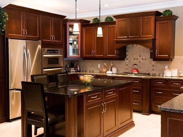 Kitchen with dark wood cabinets, stainless steel refrigerator, built-in oven, black countertop island, and three pendant lights.