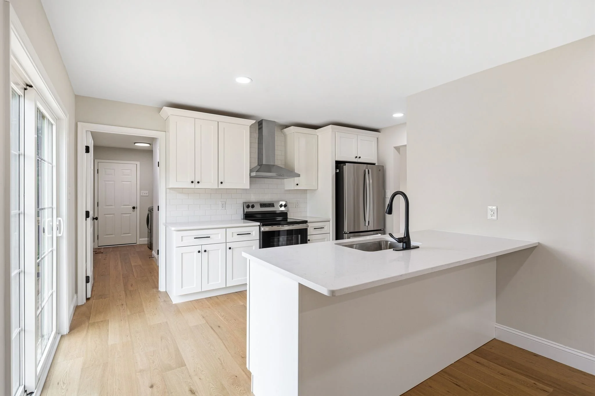 Modern kitchen with white cabinets, stainless steel stove and refrigerator, white subway tile backsplash, LVP floors, and a white countertop island with a black faucet.