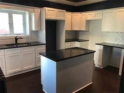Kitchen with white cabinets, black countertops, a window above the sink, and an island with a black top.