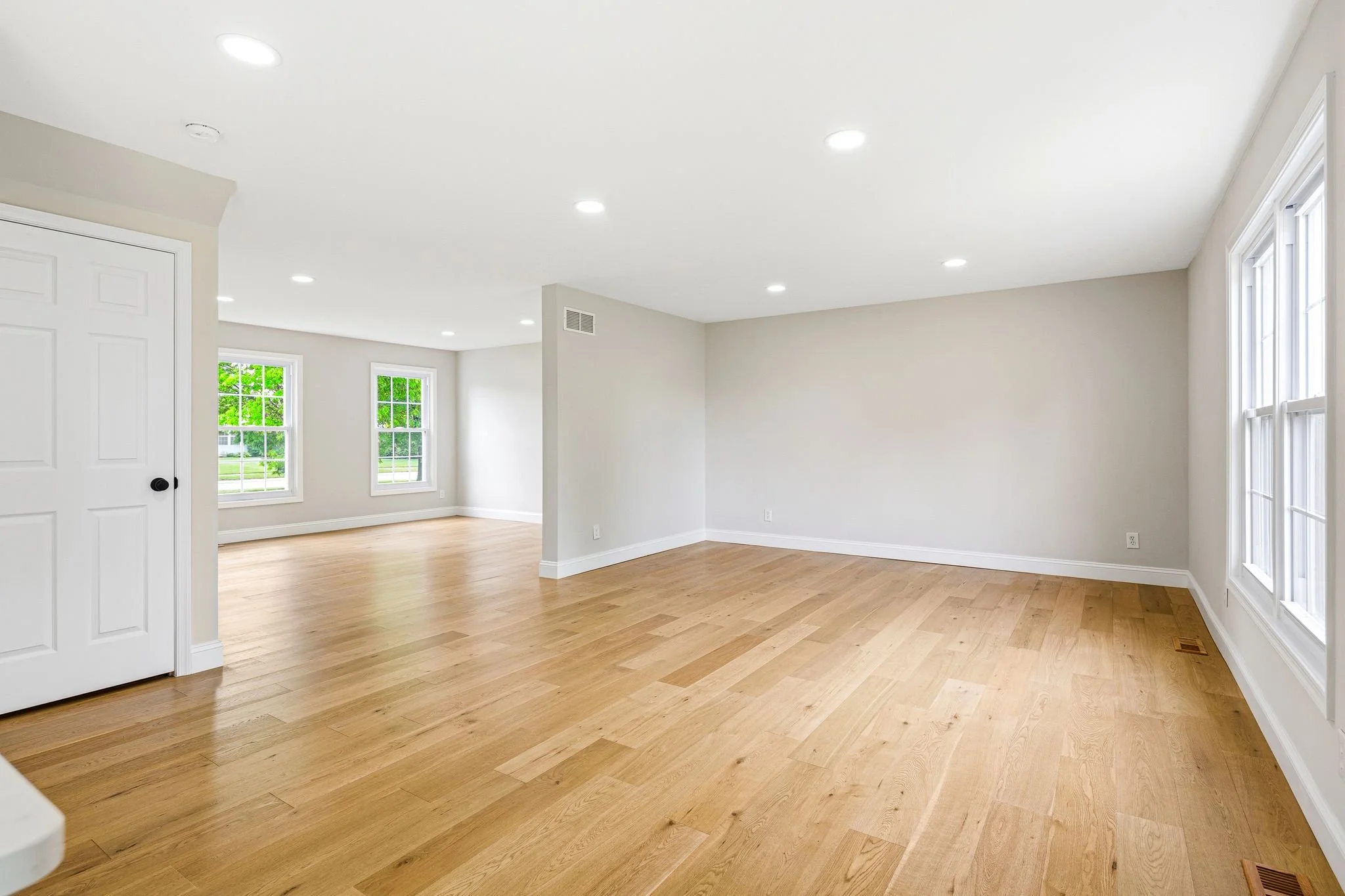 Bright, empty living room with LVP flooring, multiple large windows, and white walls.