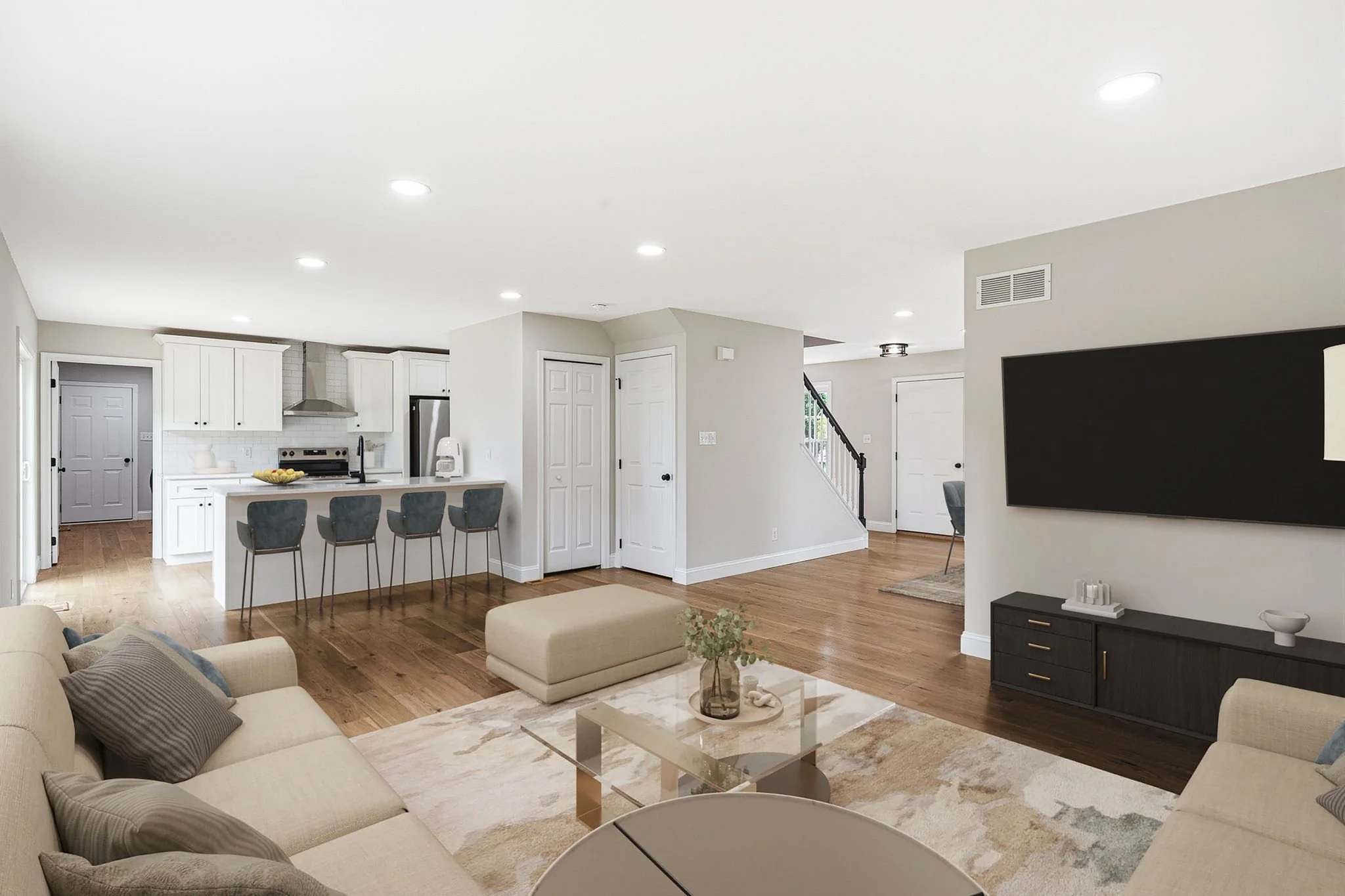 Open-concept living room and kitchen with white cabinets, gray walls, LVP flooring, and a large flat-screen TV on the wall.