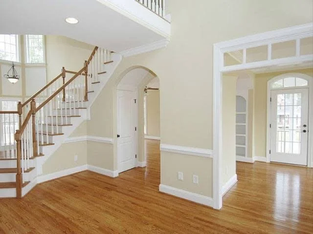 Empty living room with a wooden staircase, hardwood floors, and light-colored walls with white trim.