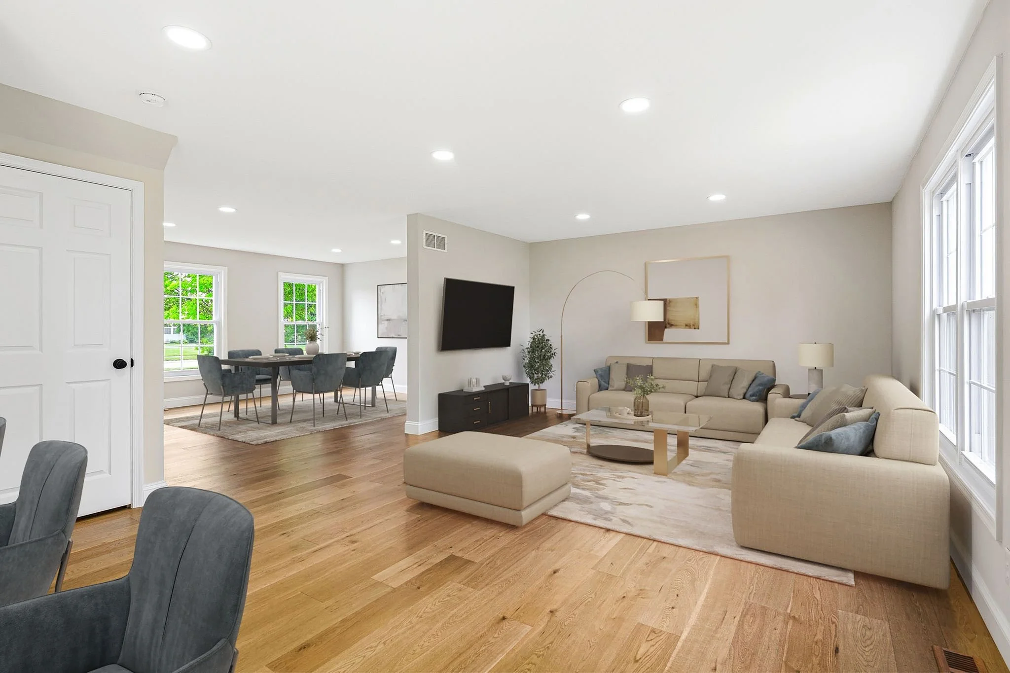 Open-concept living and dining areas with beige sofas, a wall-mounted TV, dining table with chairs, large windows, and LVP flooring.