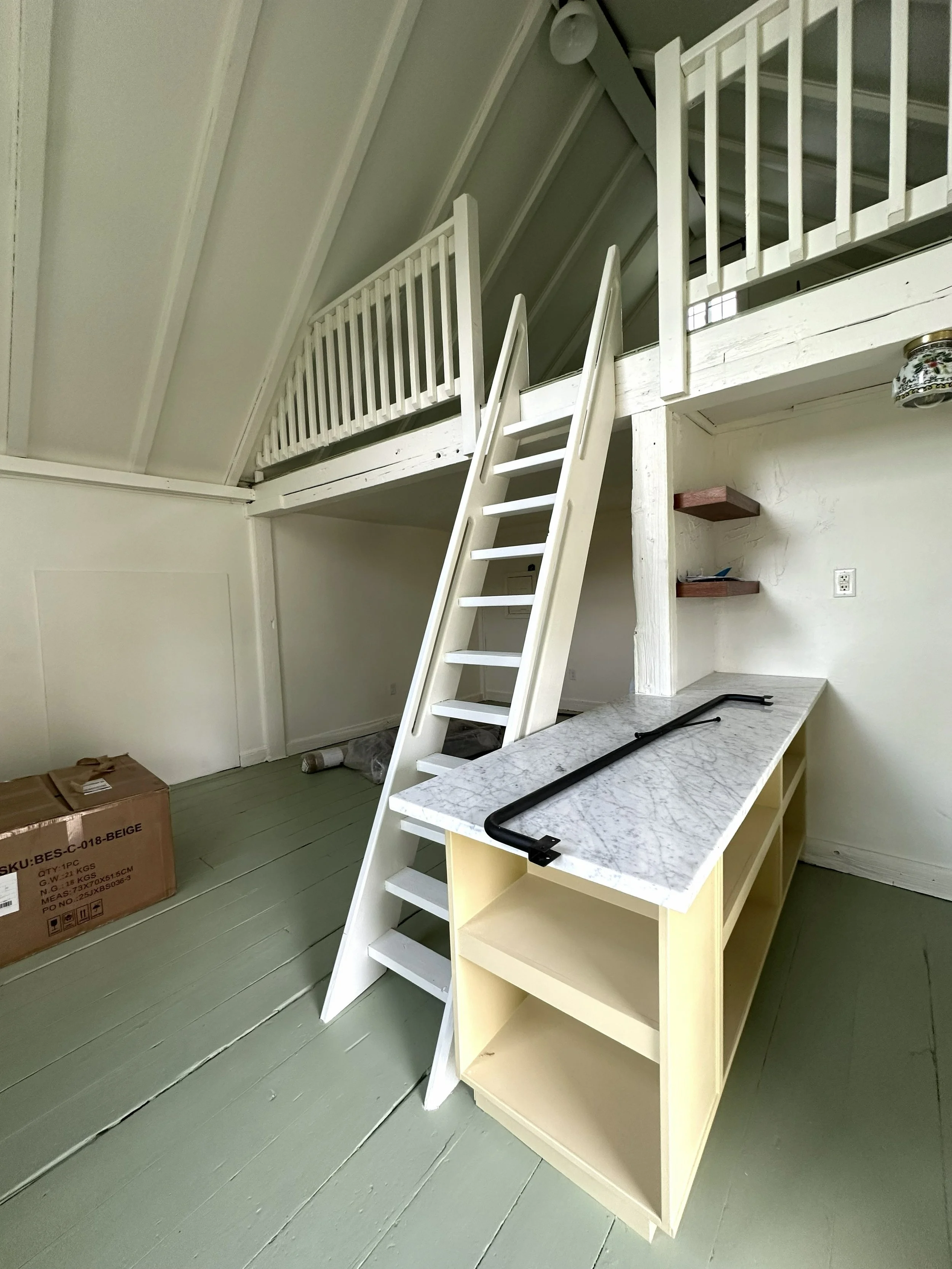 Interior view of a room with a loft area, white staircase, and a marble-topped yellow sideboard.