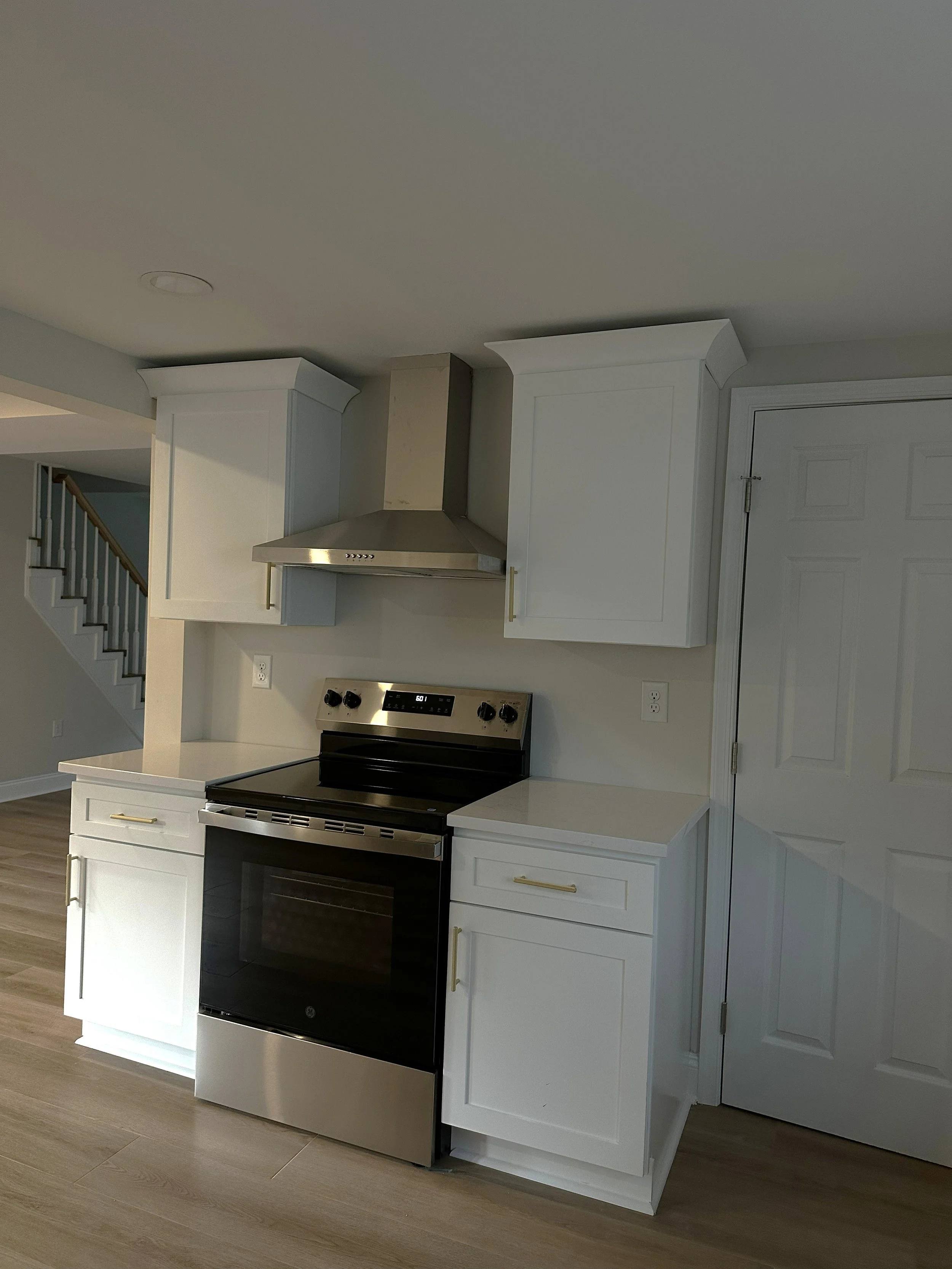 Kitchen with white cabinets, a stainless steel oven, and an electric stove, light LVP flooring, and a staircase in the background.