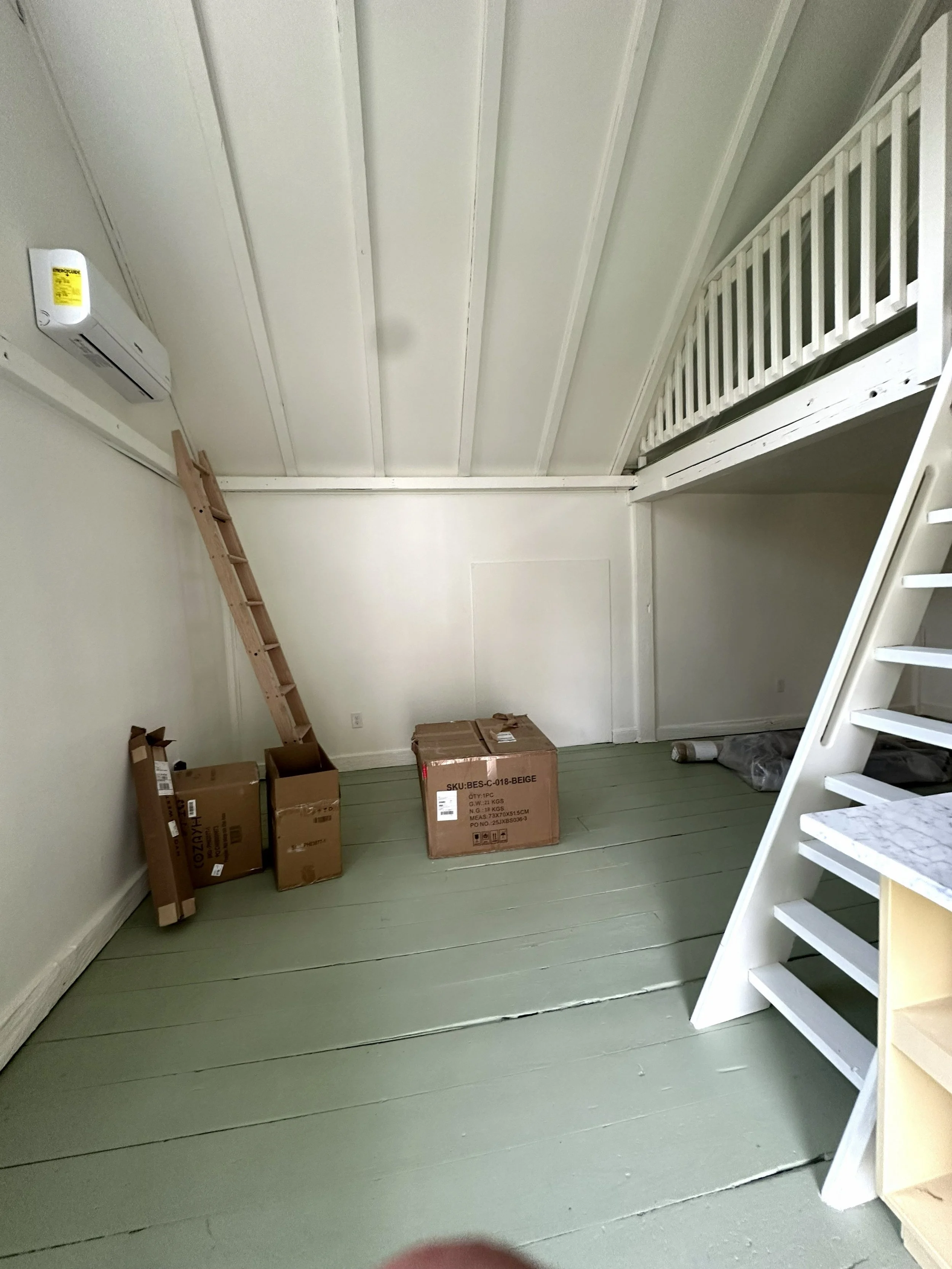 Empty room with green painted wooden floor, white walls and a white staircase with a marble top on the right side.