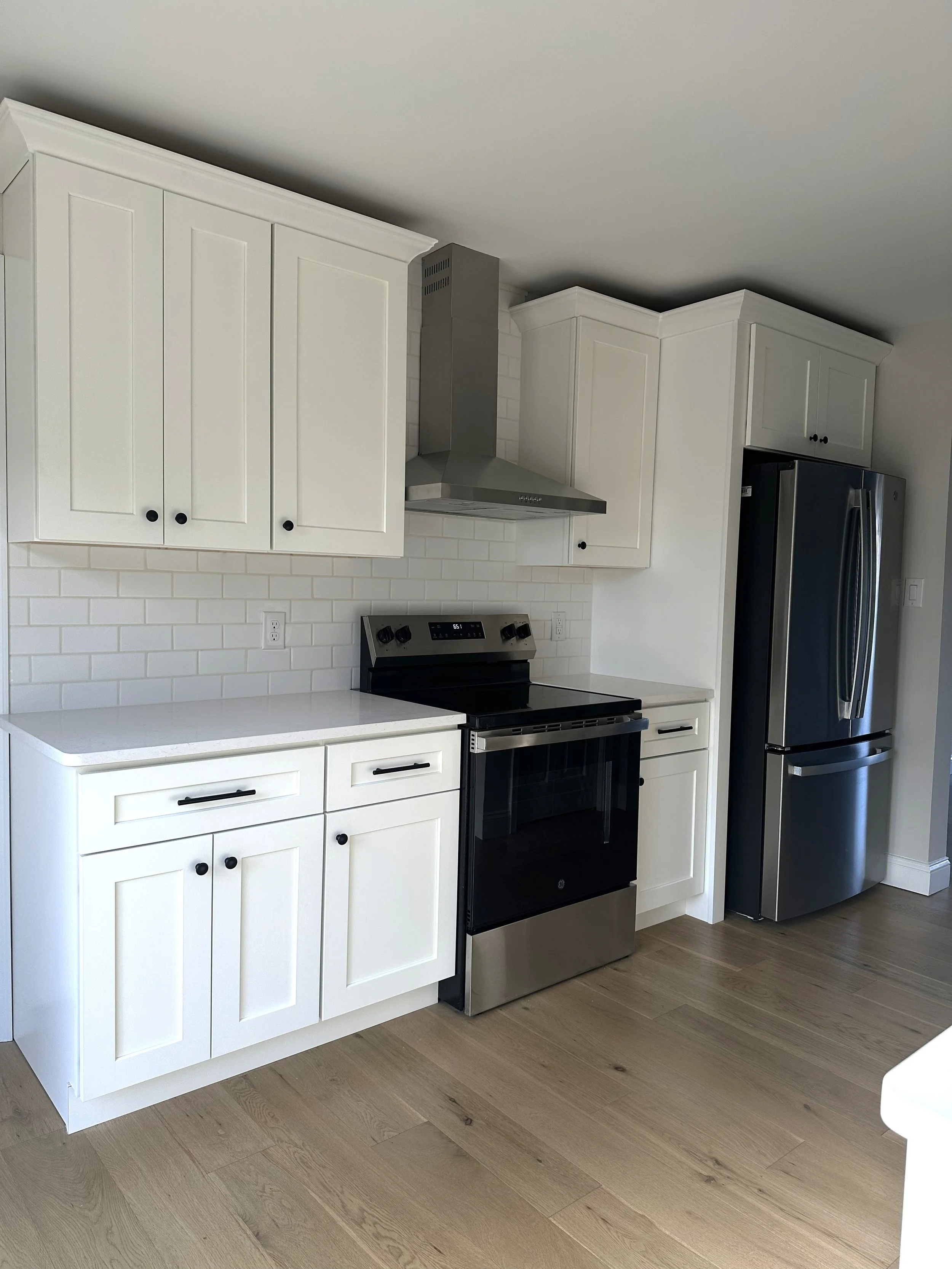 A modern kitchen with white cabinets, a gray stove, a stainless steel refrigerator, and LVP flooring.