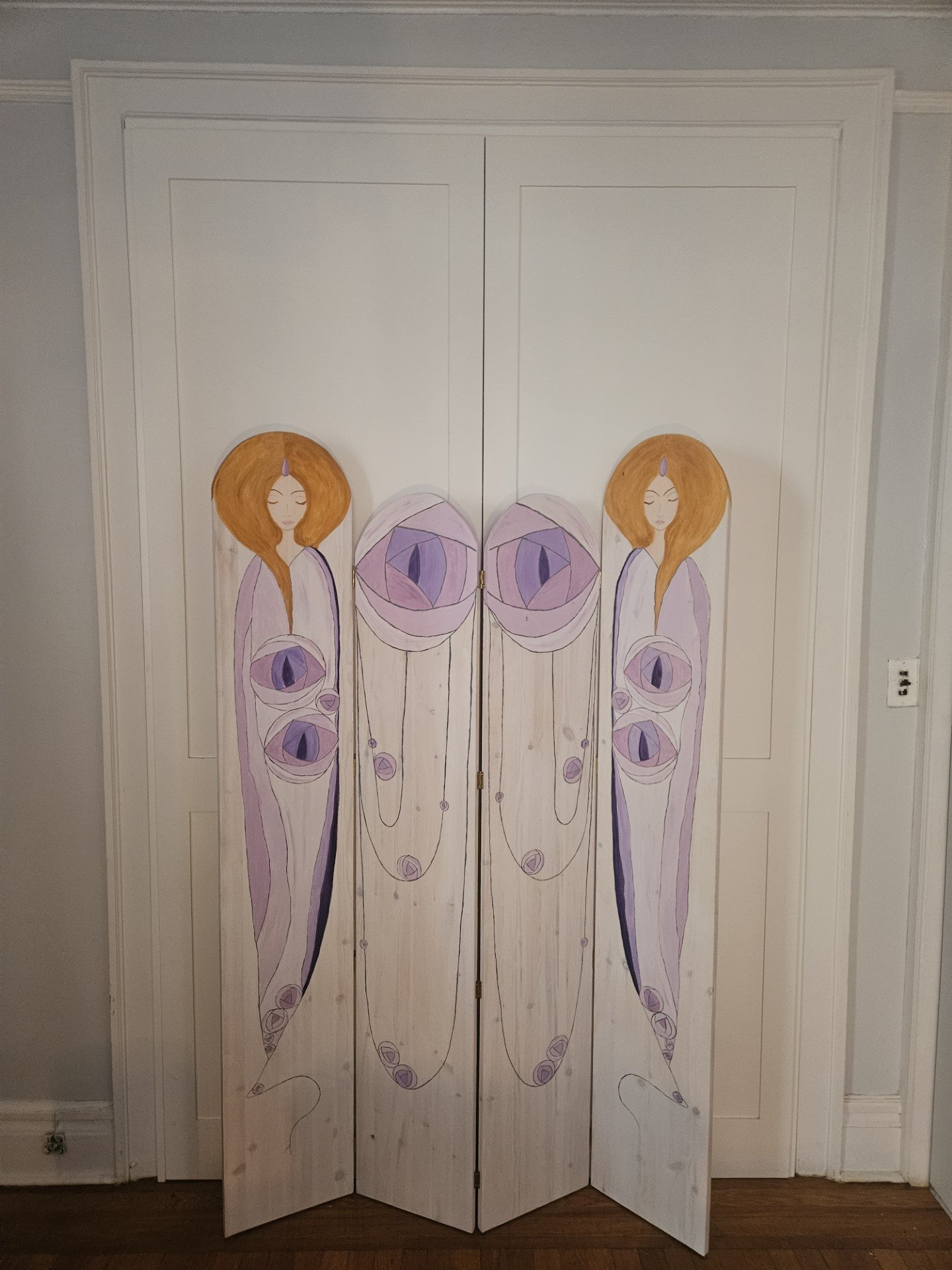 Decorated wooden closet doors featuring artwork of two women with long hair and hypnotic eye designs on their bodies in pastel purple, brown, and black colors.