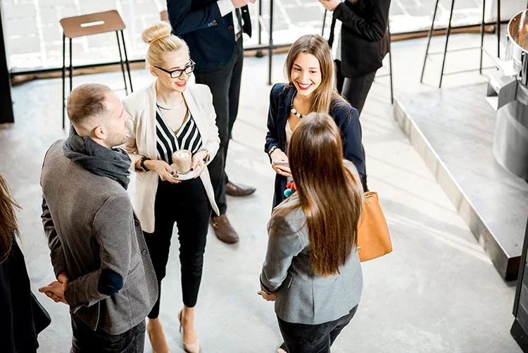 Four people, two women and two men, are standing in a circle engaged in conversation at a social gathering or networking event.