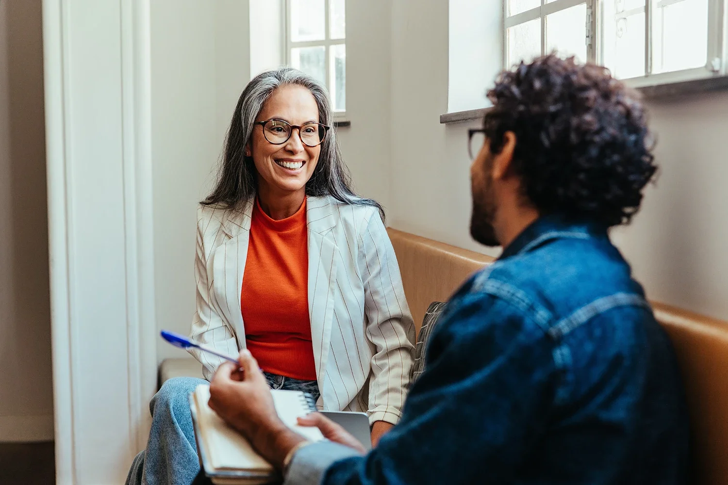 A woman with gray hair, glasses, and a striped blazer smiles during a consultation with a KCUR sponsorship representative.