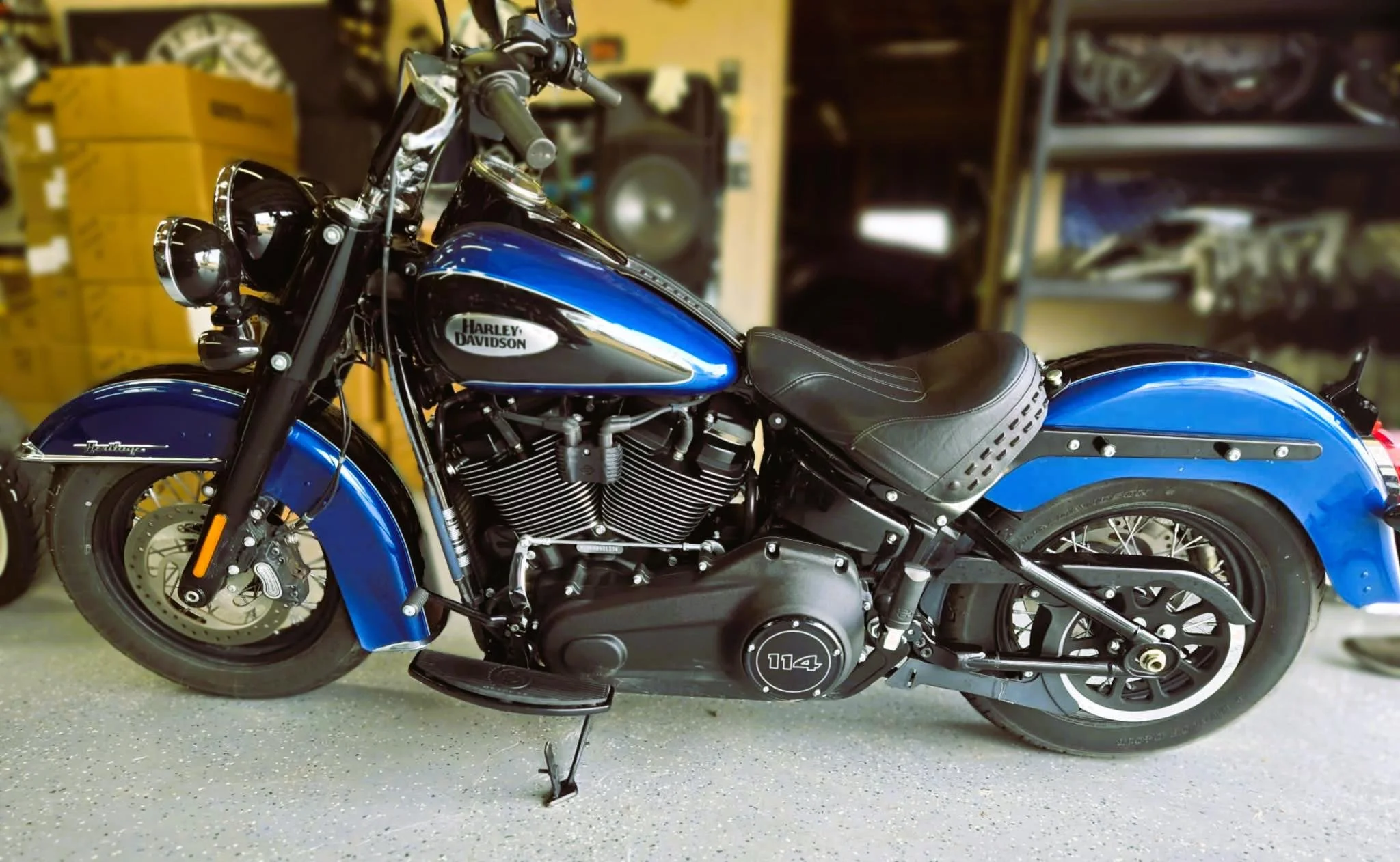 A blue Harley Davidson motorcycle in a garage or workshop, with shelves and boxes in the background.