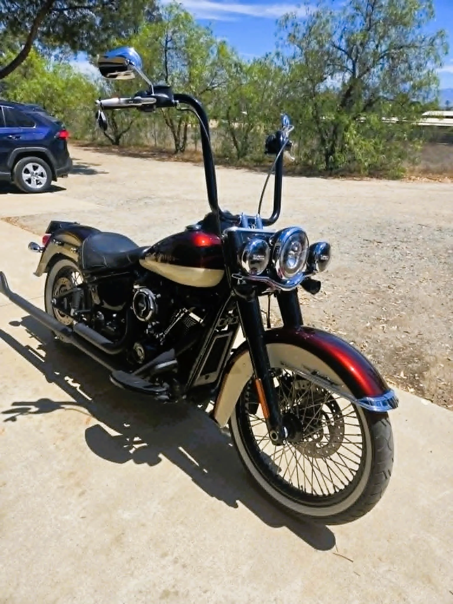 A black and red motorcycle parked on a concrete surface with trees and a blue sky in the background.