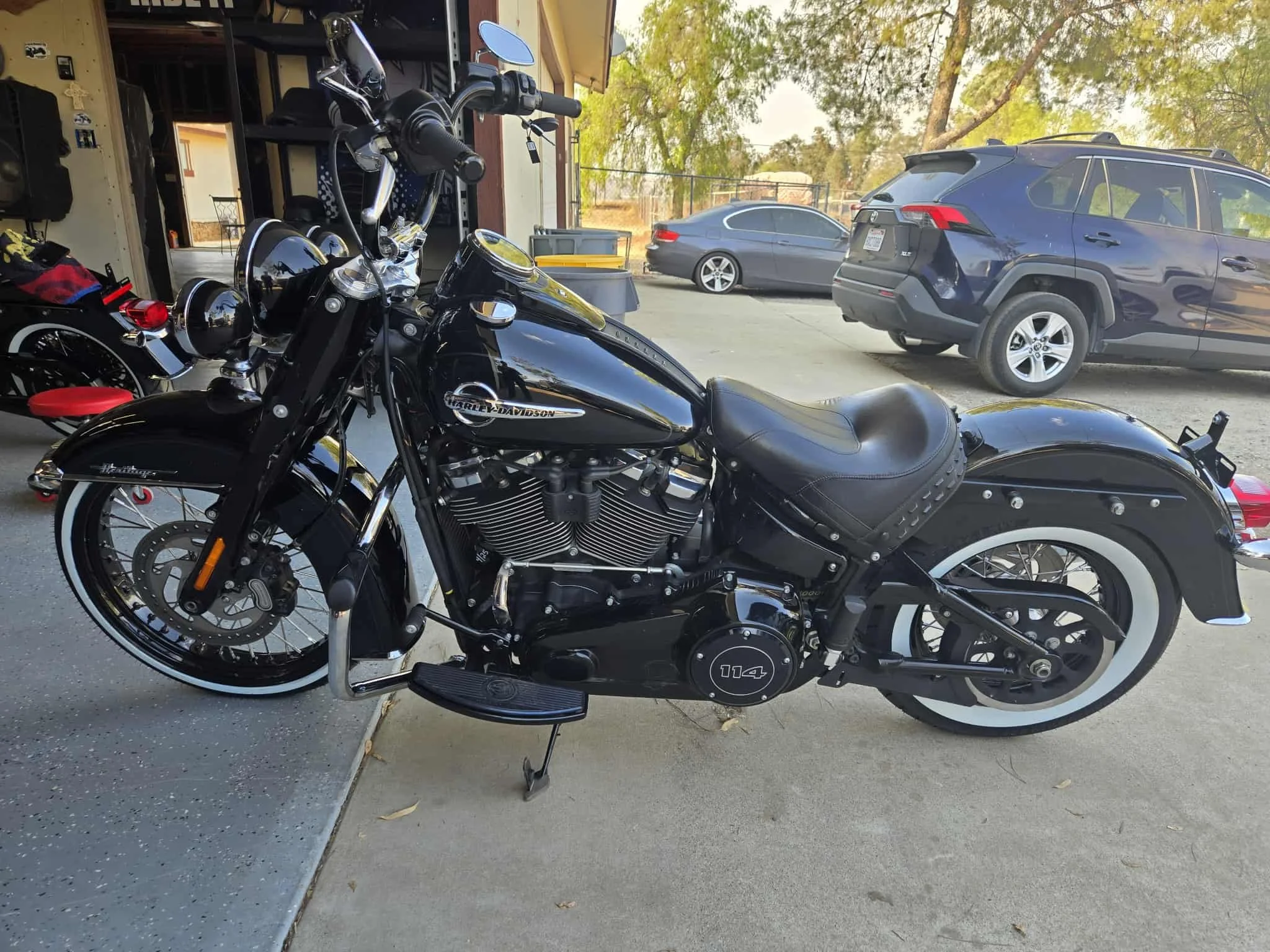 Black Harley-Davidson motorcycle parked outside a garage, with cars and trees in the background.