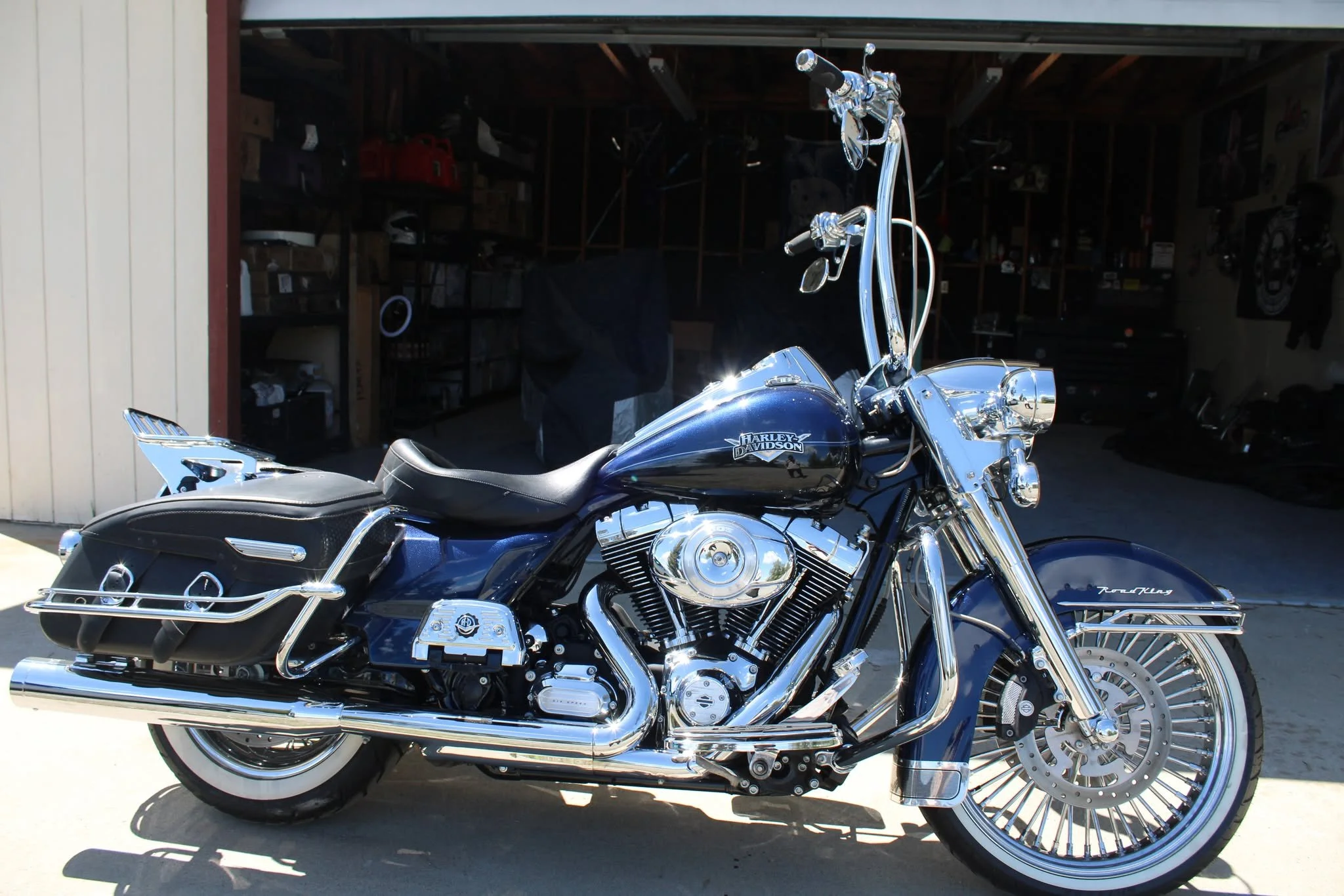 A shiny black and chrome Harley Davidson motorcycle parked outside a garage.